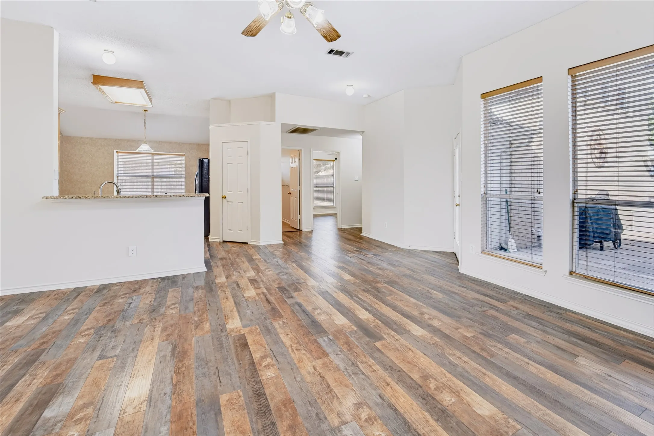 Open-concept interior featuring wood-finish flooring, a kitchen breakfast bar with stone-finish countertops, natural light through multi-pane windows, and a ceiling-mounted light fixture