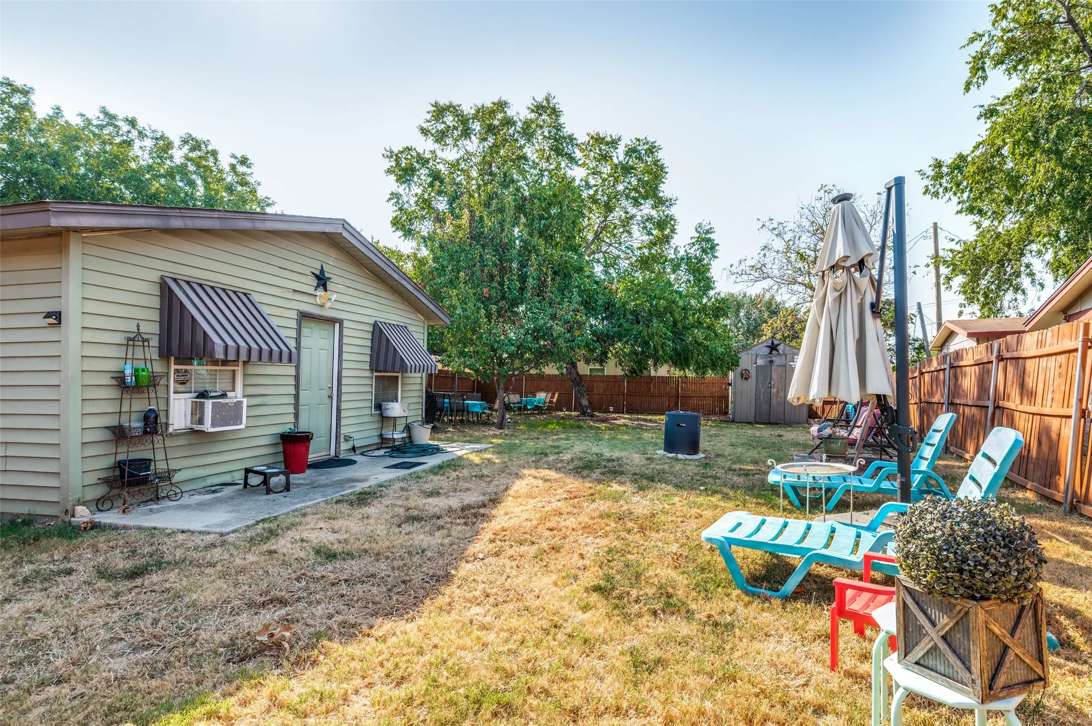 Expansive backyard with a wooden fence, mature trees, a storage shed, and a quaint concrete patio