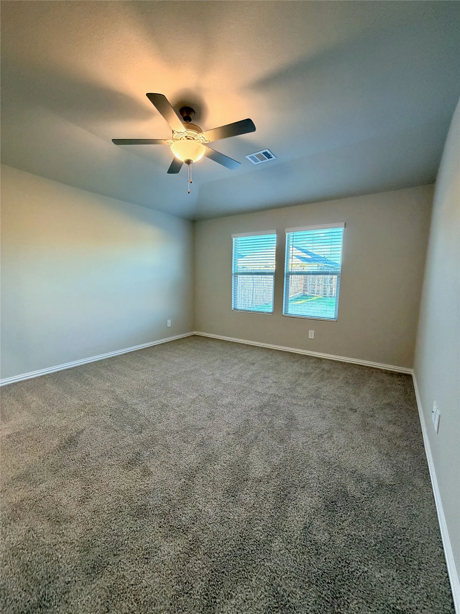 Neutral-toned walls, two windows with blinds, ceiling fan with integrated lighting, and wall-to-wall carpeting