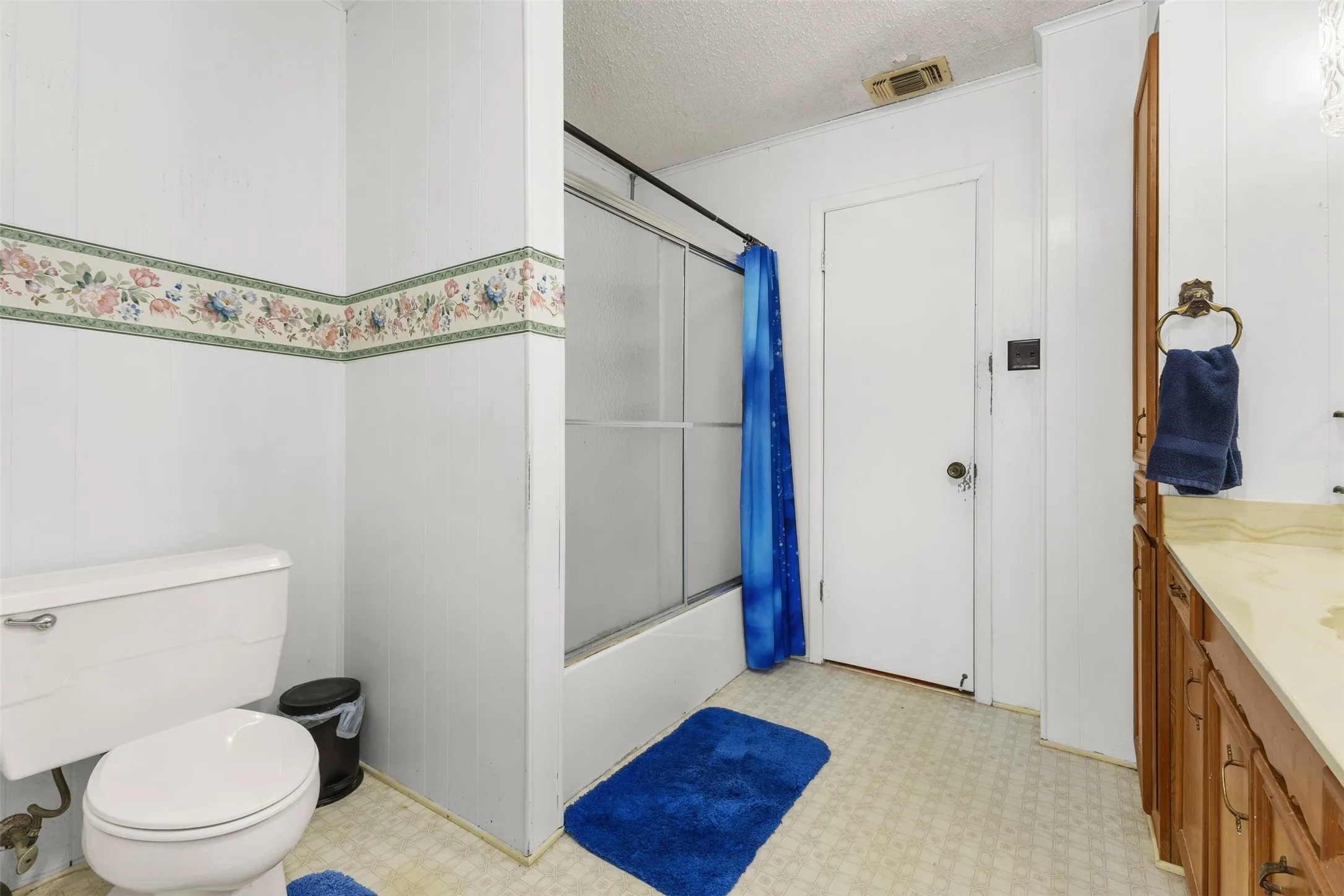 White paneled walls with decorative border, white toilet, shower with sliding glass door, light wood-finish vanity with countertop