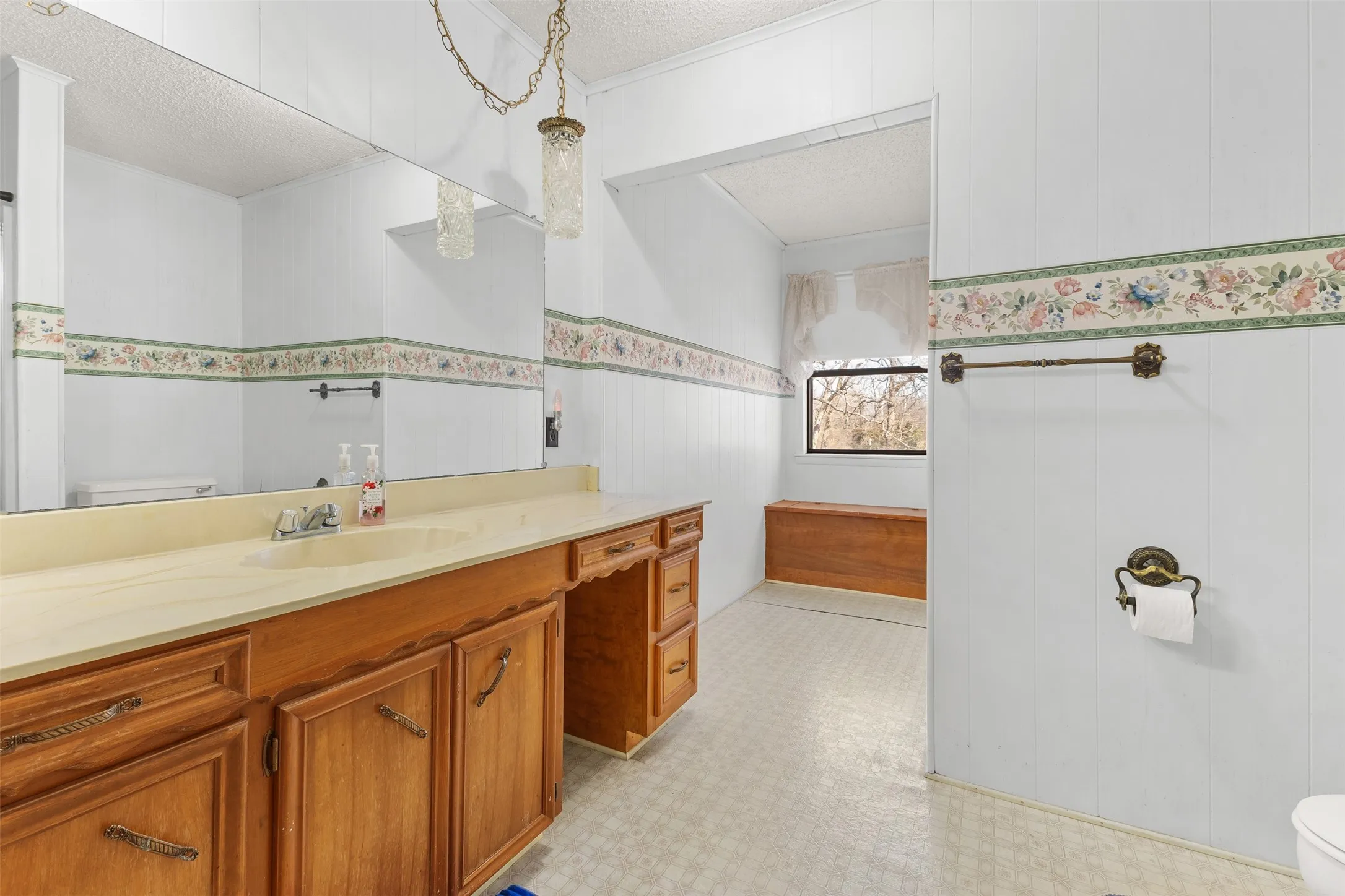 Extended vanity with a built-in sink, wood-finish cabinetry, and a large wall-mounted mirror