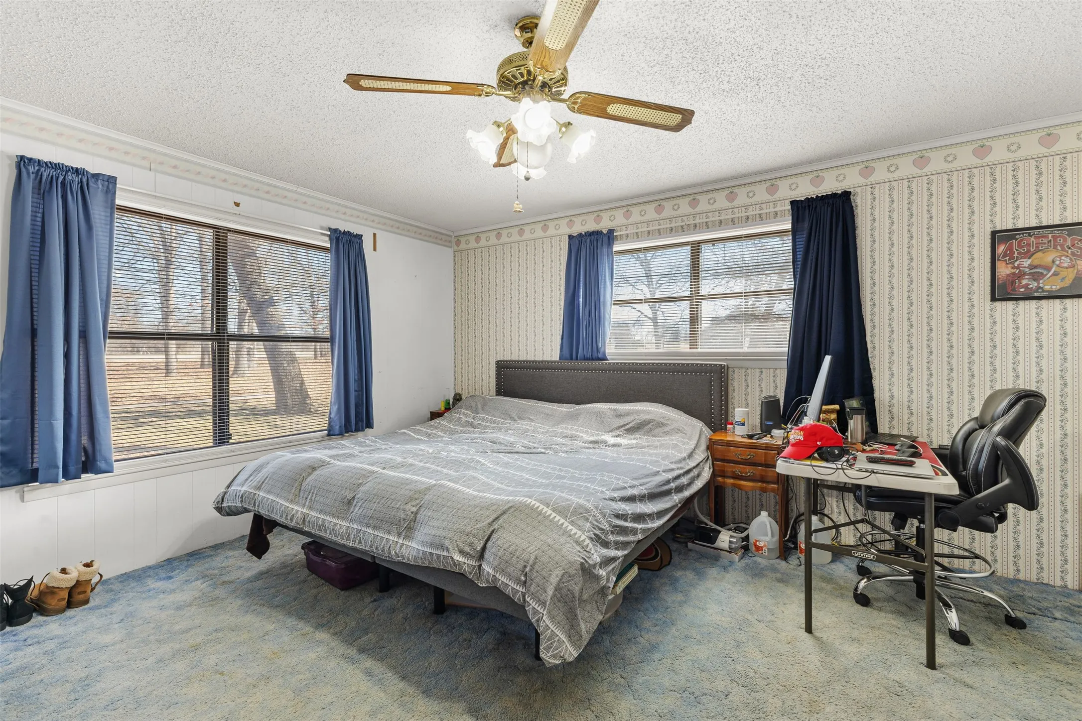 Ceiling fan with light fixture, multiple windows, textured ceiling, and patterned wallpaper