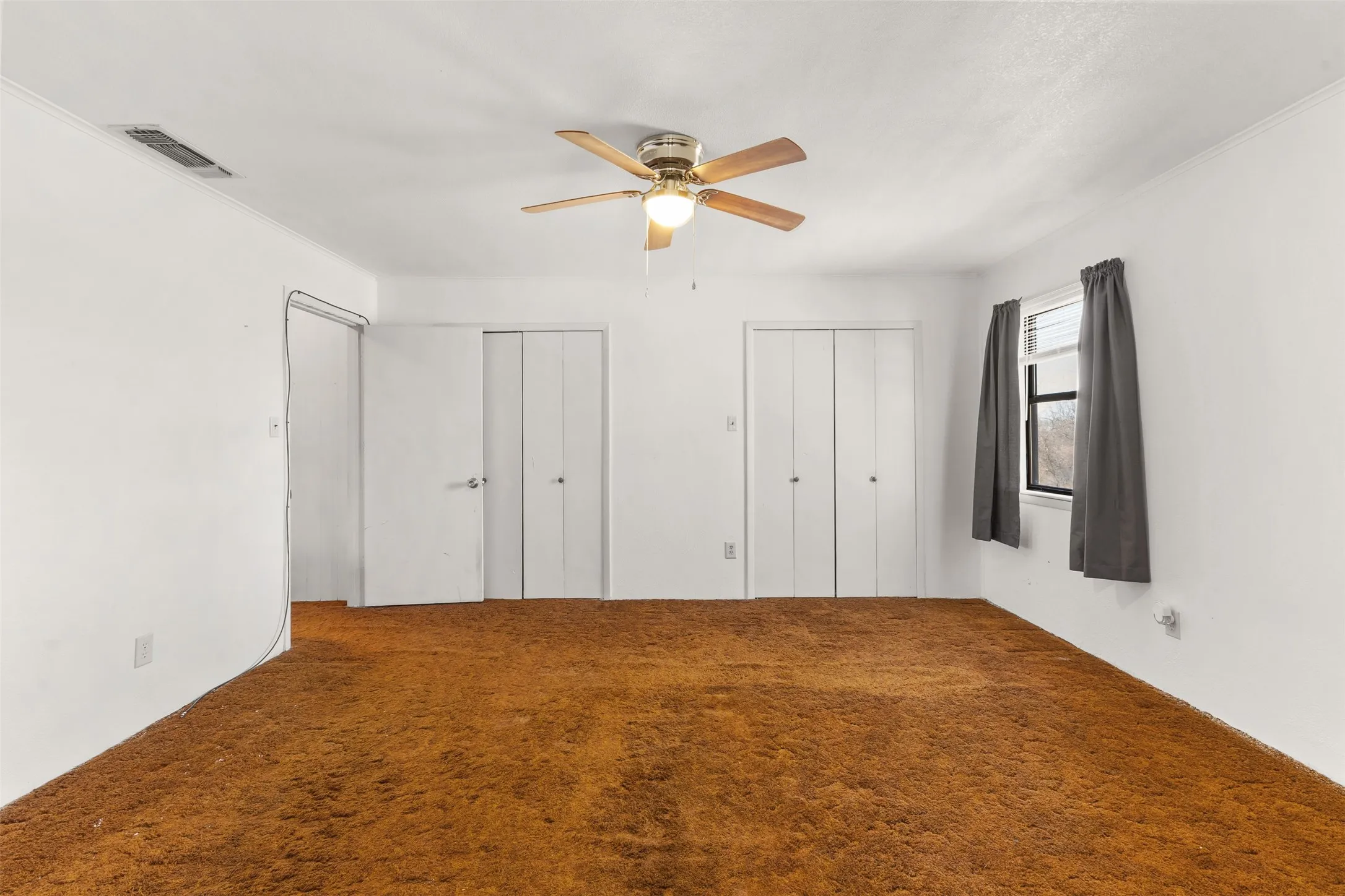 Ceiling fan with light fixture, multiple closet doors, and window with natural light