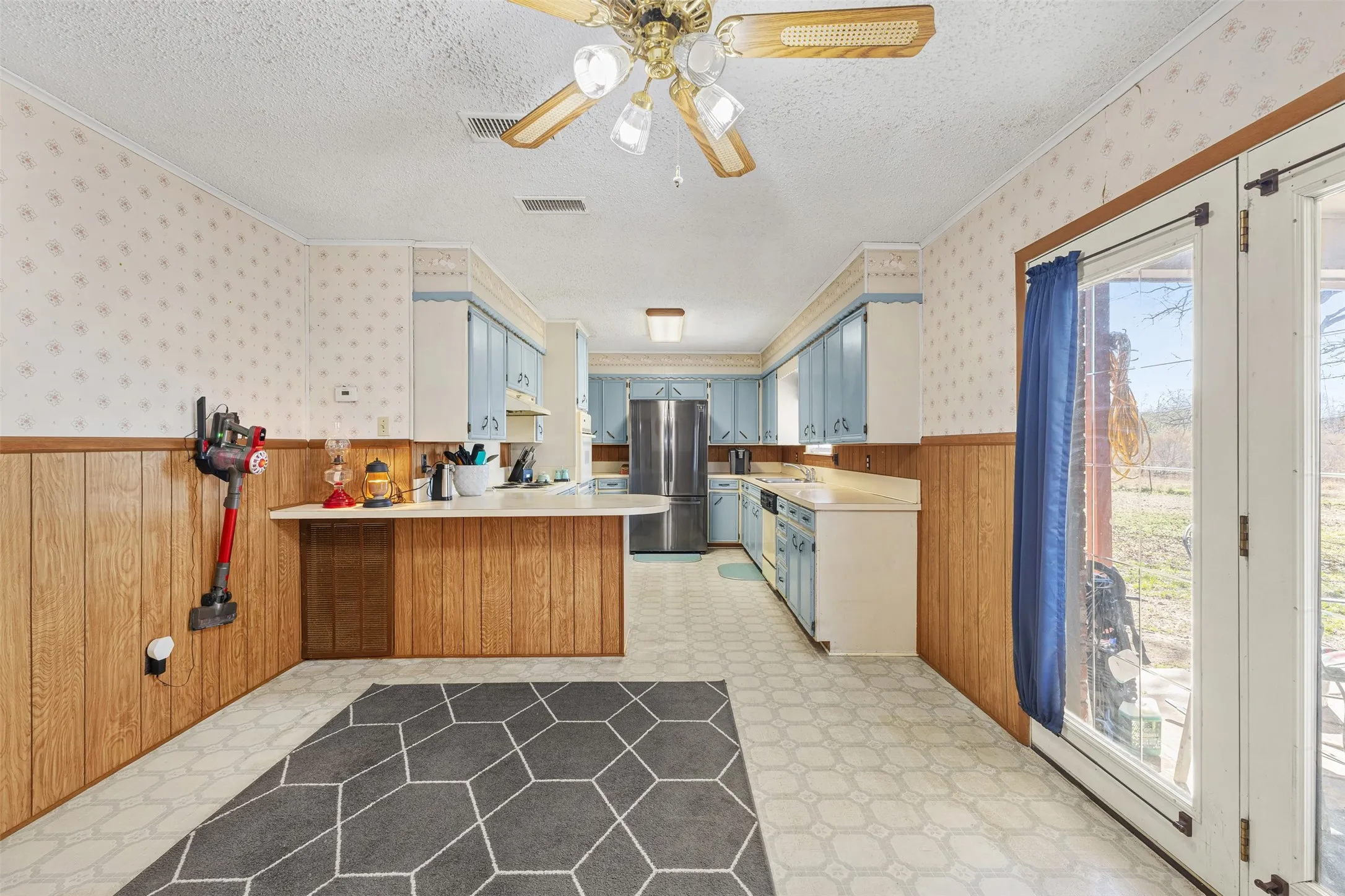 Kitchen featuring ceiling fan, wood-paneled walls, light blue cabinetry, and double glass-paneled doors