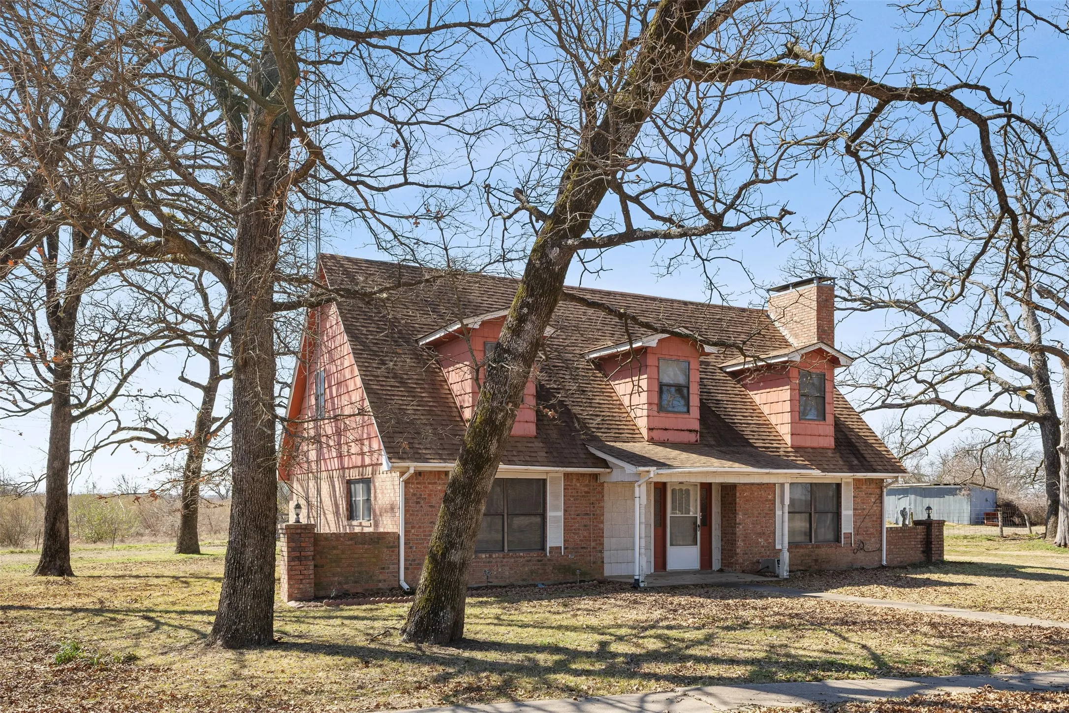 Brick and shingle exterior with dormer windows, a covered front porch, and a brick chimney