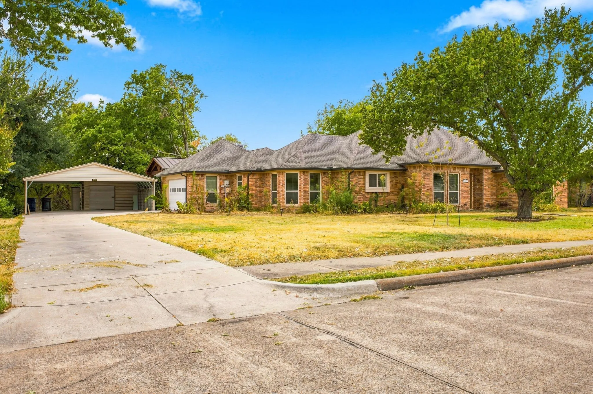Brick exterior, attached garage, covered carport, concrete driveway, mature trees