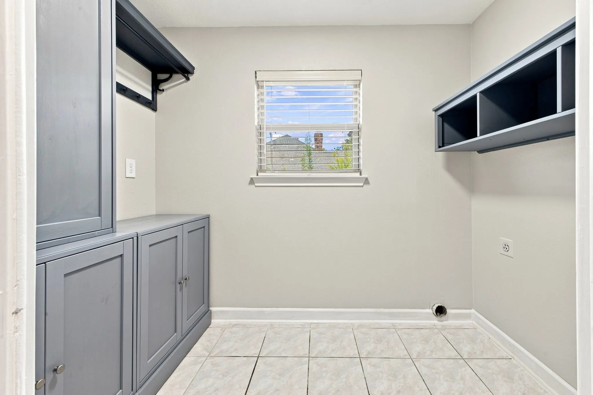 Built-in cabinetry, overhead shelving, window with blinds, and tiled flooring