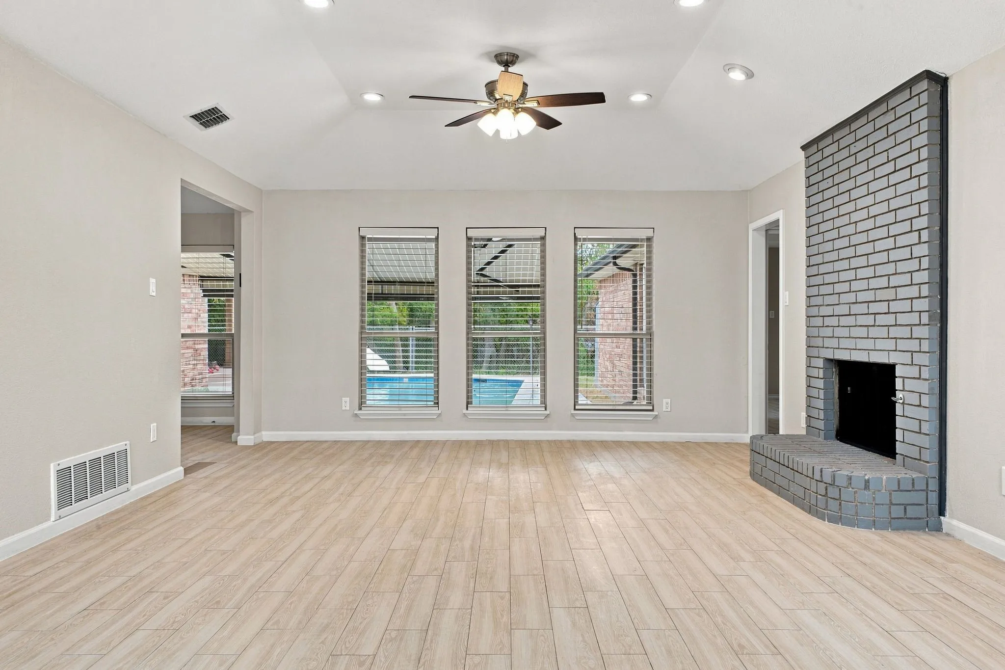 Vaulted ceiling with recessed lighting and ceiling fan, wood-finish flooring, brick fireplace, and multiple windows with horizontal blinds