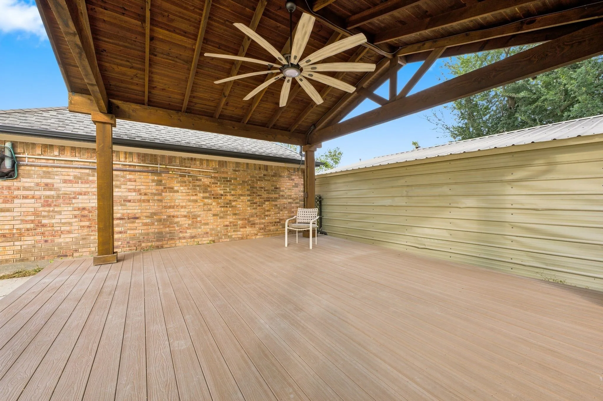 Expansive covered patio featuring a wood-finish deck, exposed wood beams, and a ceiling fan
