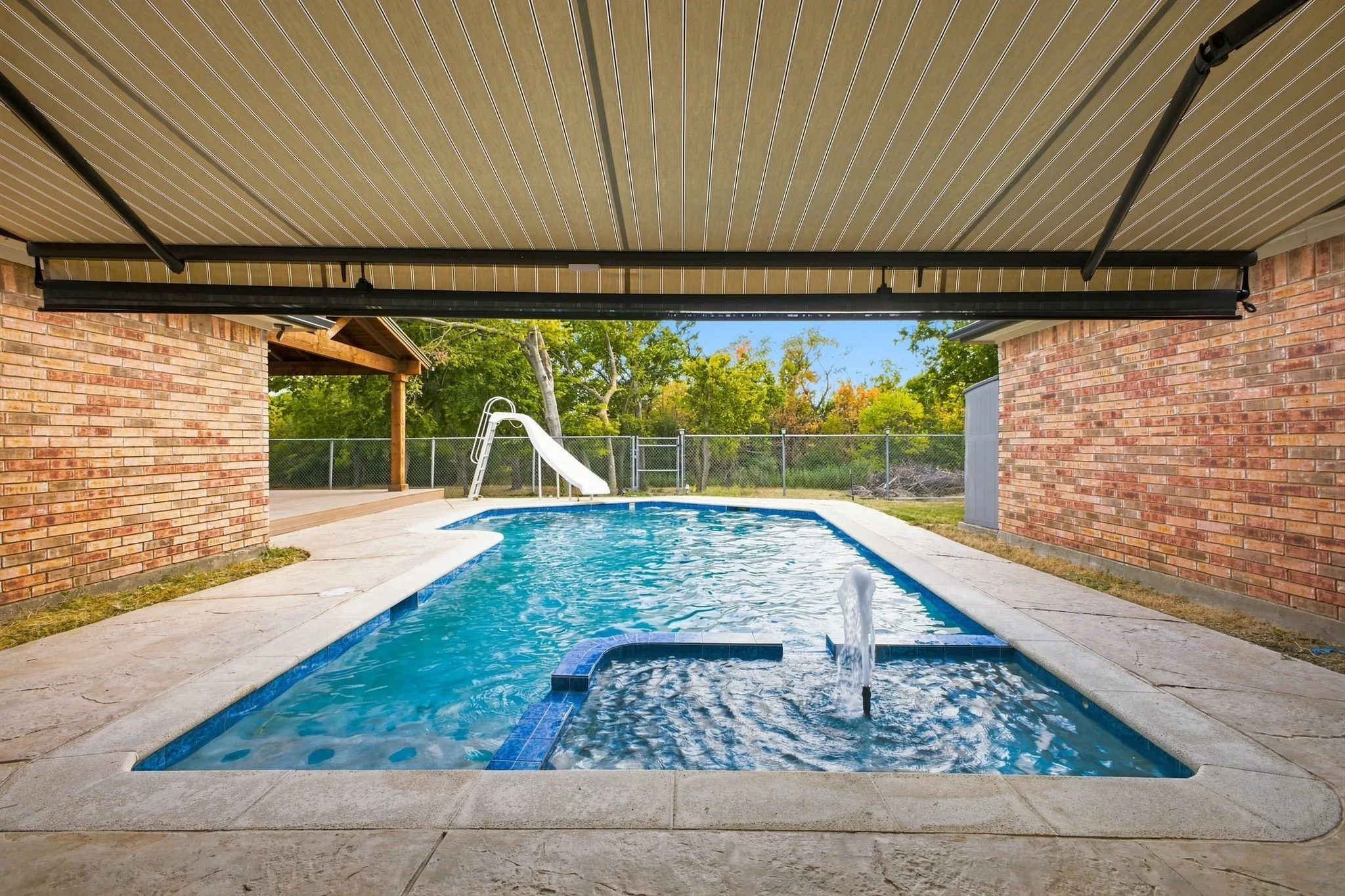 Covered swimming pool featuring an integrated spa with water feature, concrete decking, and brick exterior walls