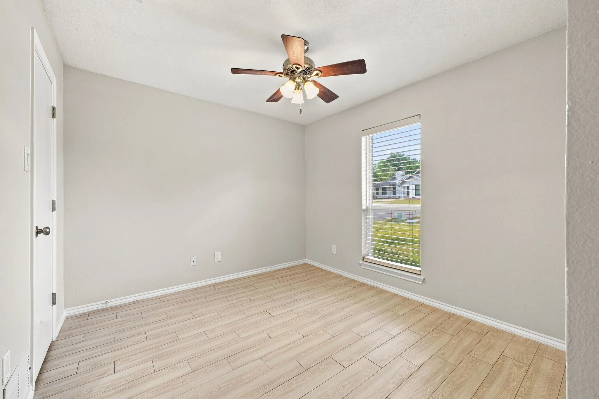 Neutral wall paint, wood-finish flooring, ceiling fan, window with blinds, and white trim