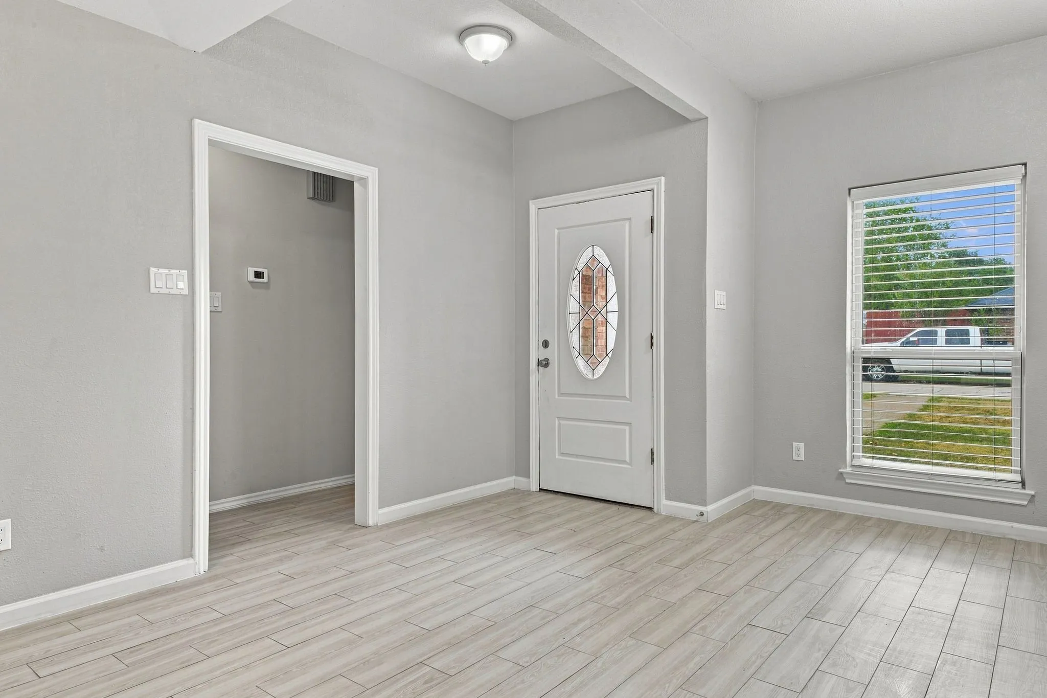 Light gray walls, wood-finish flooring, recessed lighting, and a front entry door with decorative glass inlay