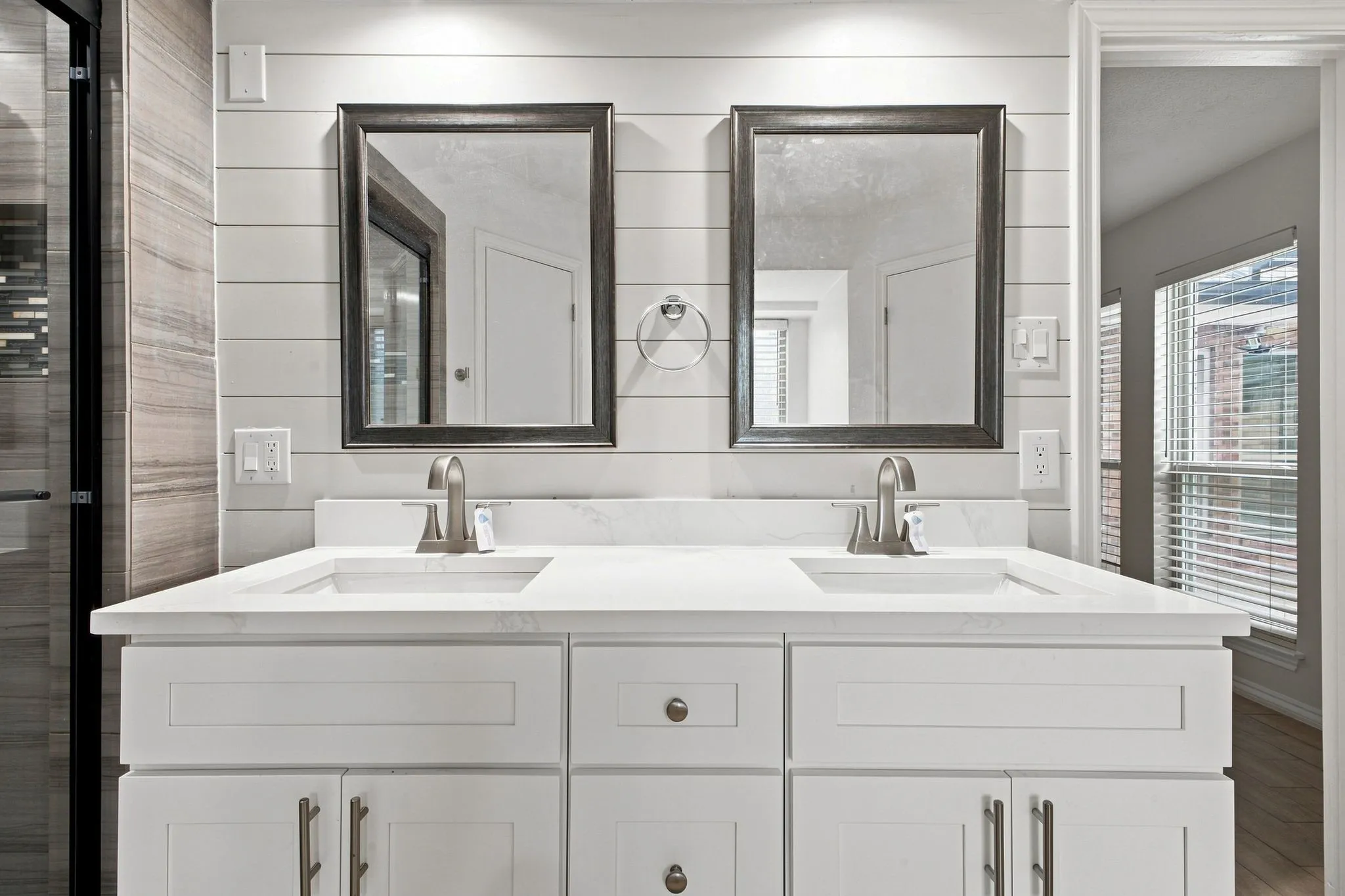 Dual vanity with white cabinetry, integrated sinks, brushed nickel faucets, and framed mirrors set against a shiplap accent wall