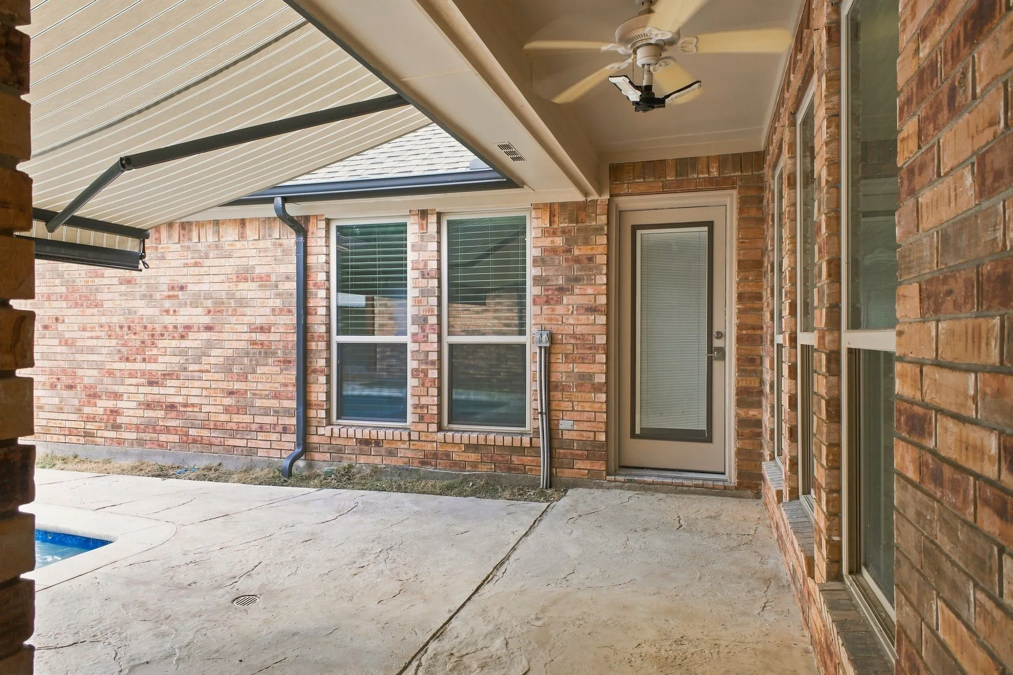 Brick exterior, covered patio, stamped concrete flooring, ceiling fan, and multiple windows