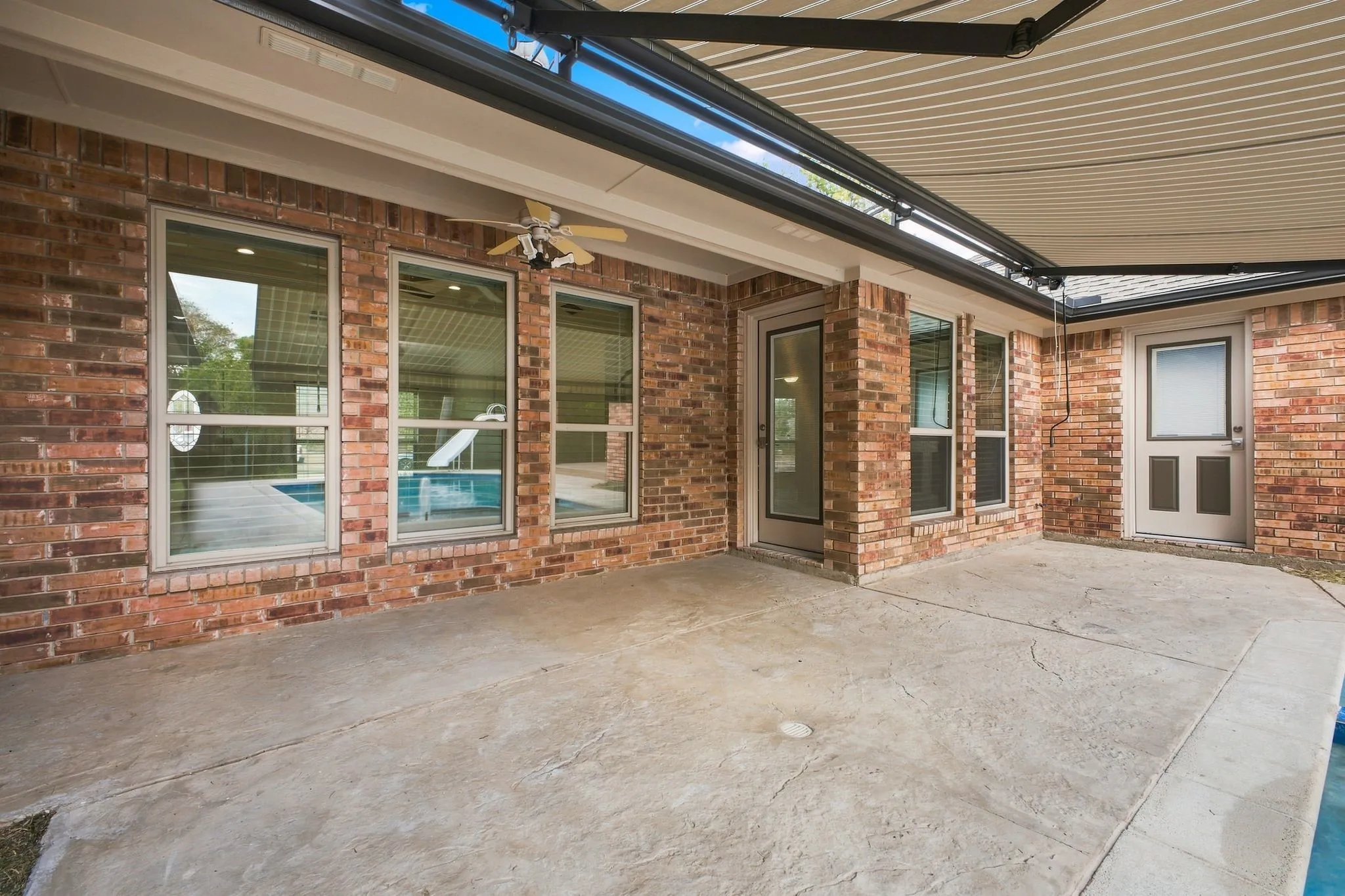 Brick exterior with a covered patio, stamped concrete flooring, and an integrated ceiling fan
