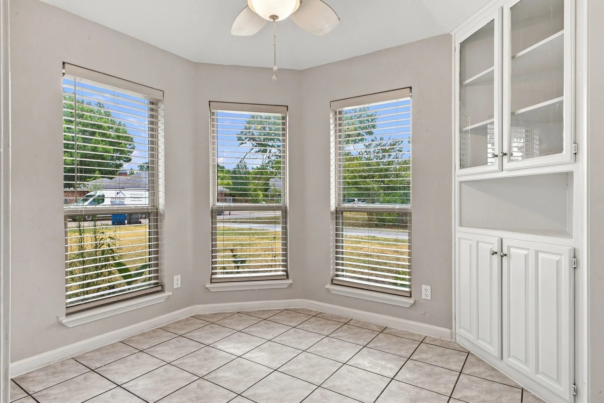 Tiled flooring, multiple windows with blinds, built-in cabinetry with glass-front uppers, and a ceiling fan