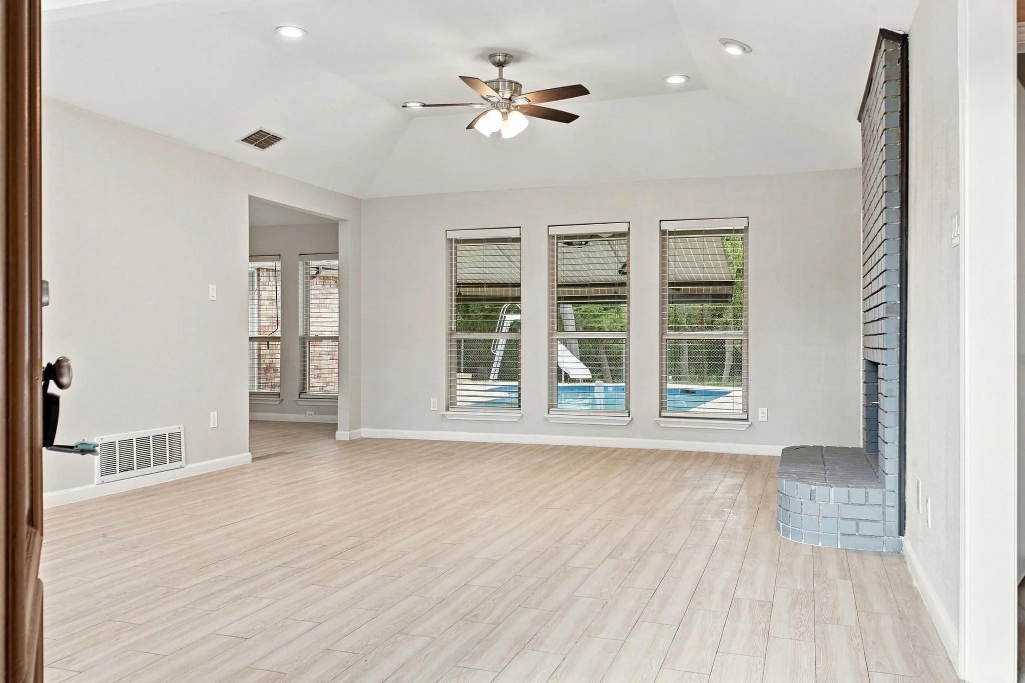 Vaulted ceiling with recessed lighting, ceiling fan, wood-finish flooring, brick fireplace, and multiple windows