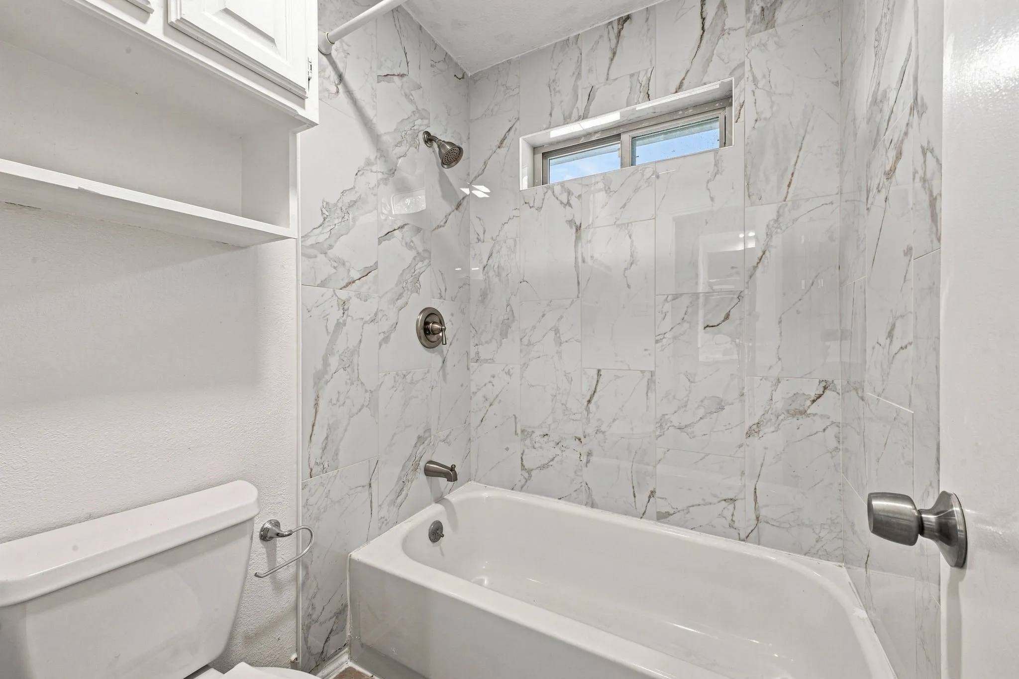 Bathtub with a shower fixture, white tiled surround, and transom window