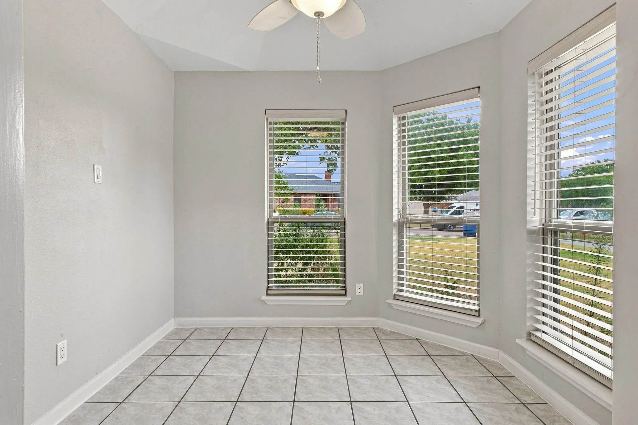 Recessed bay window area featuring three windows with blinds, ceramic tile flooring, and a ceiling fan