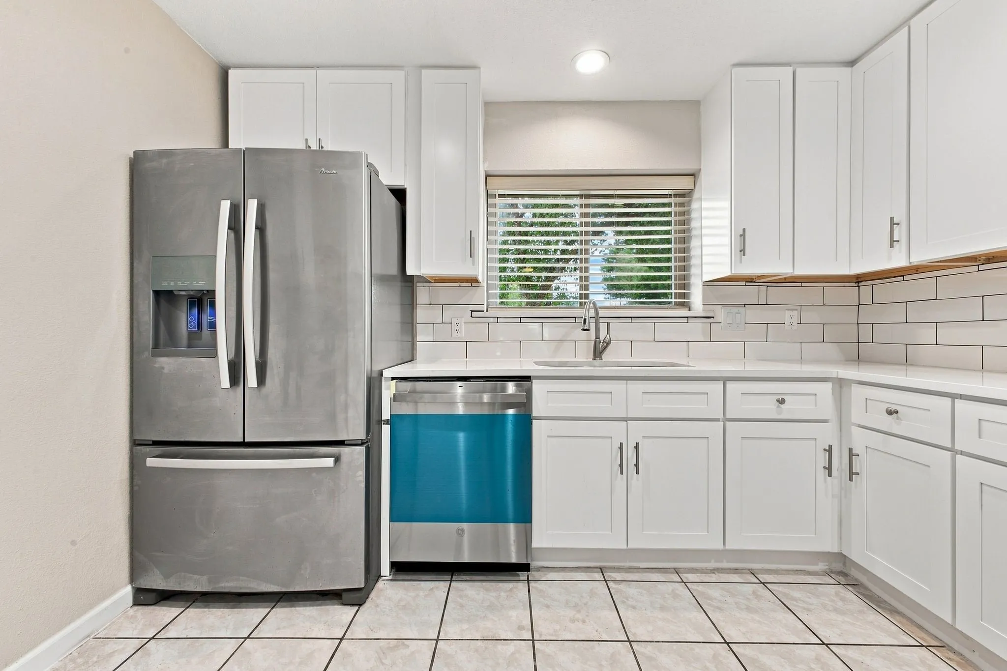 White shaker-style cabinetry, white subway tile backsplash, light-toned countertops, and square tile flooring