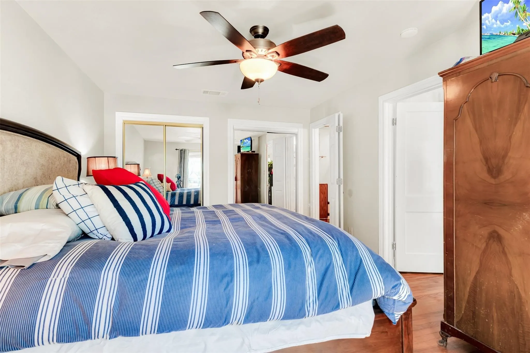 Ceiling fan with integrated lighting, wood-finish flooring, white walls, and a mirrored closet