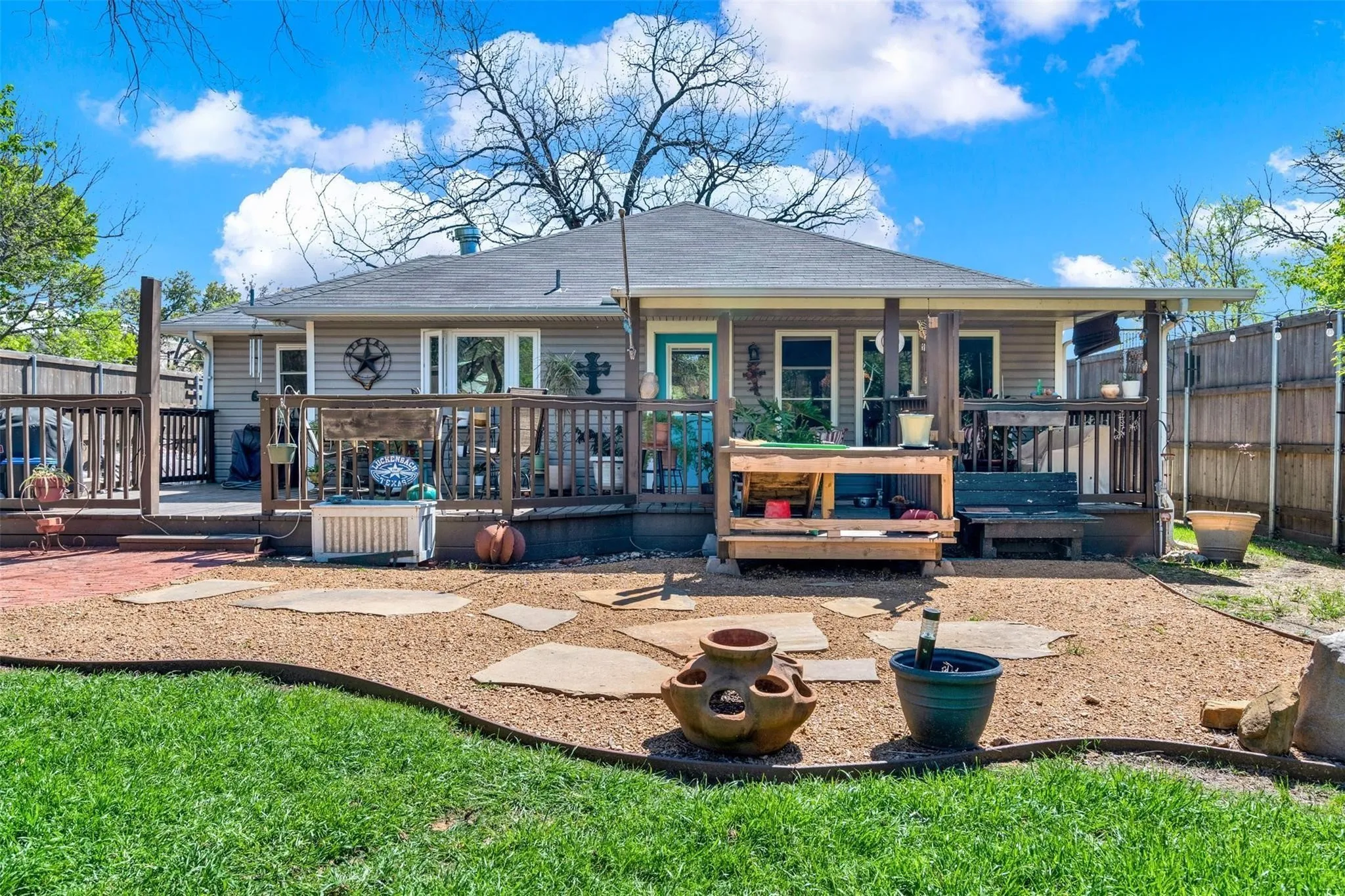 Expansive wooden deck with railing, covered patio area, gravel hardscaping with stone pavers, and a manicured lawn