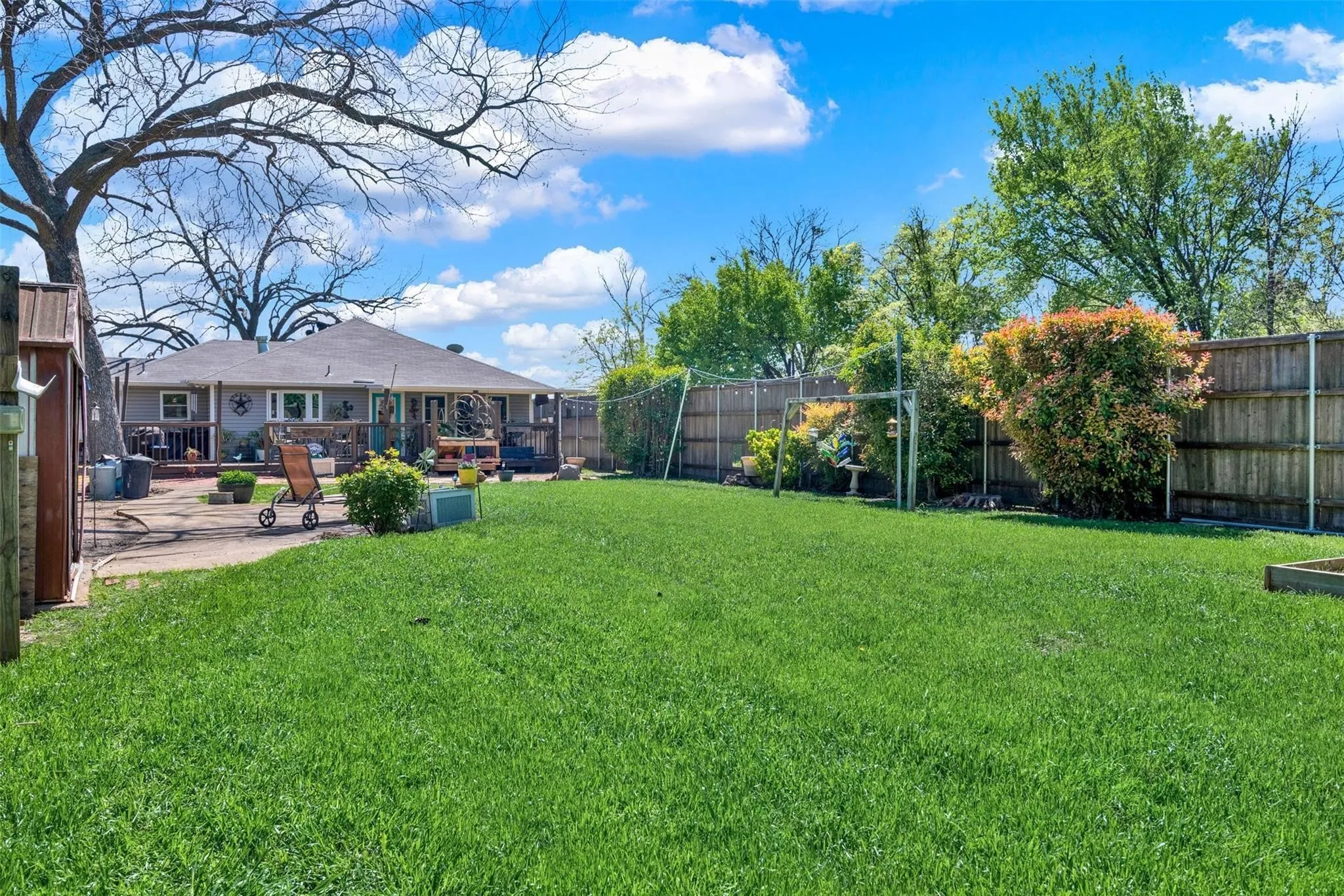 Expansive backyard with a manicured lawn, wood fencing, mature trees, and a concrete patio