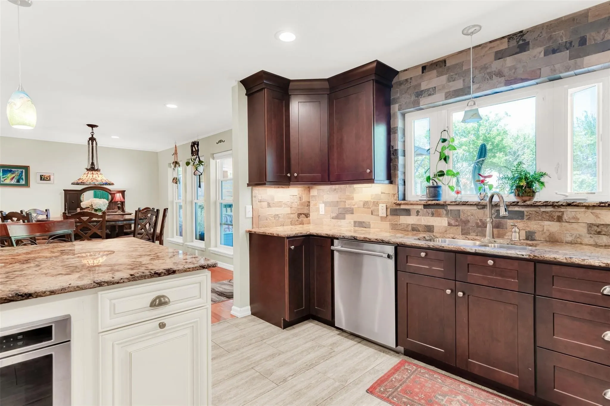 Kitchen featuring wood-finish cabinetry, stone countertops, stone tile backsplash, stainless steel appliances, and tile flooring