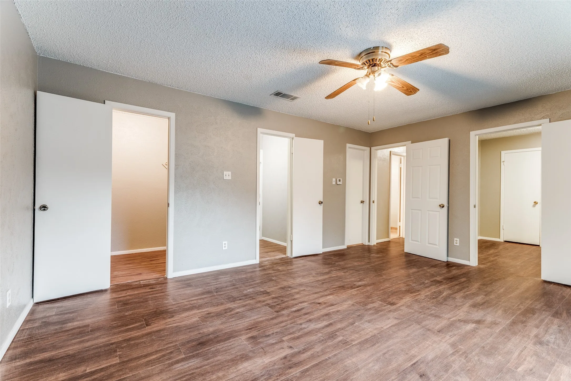Spacious room featuring wood-finish flooring, neutral-toned walls, and a ceiling fan with integrated lighting