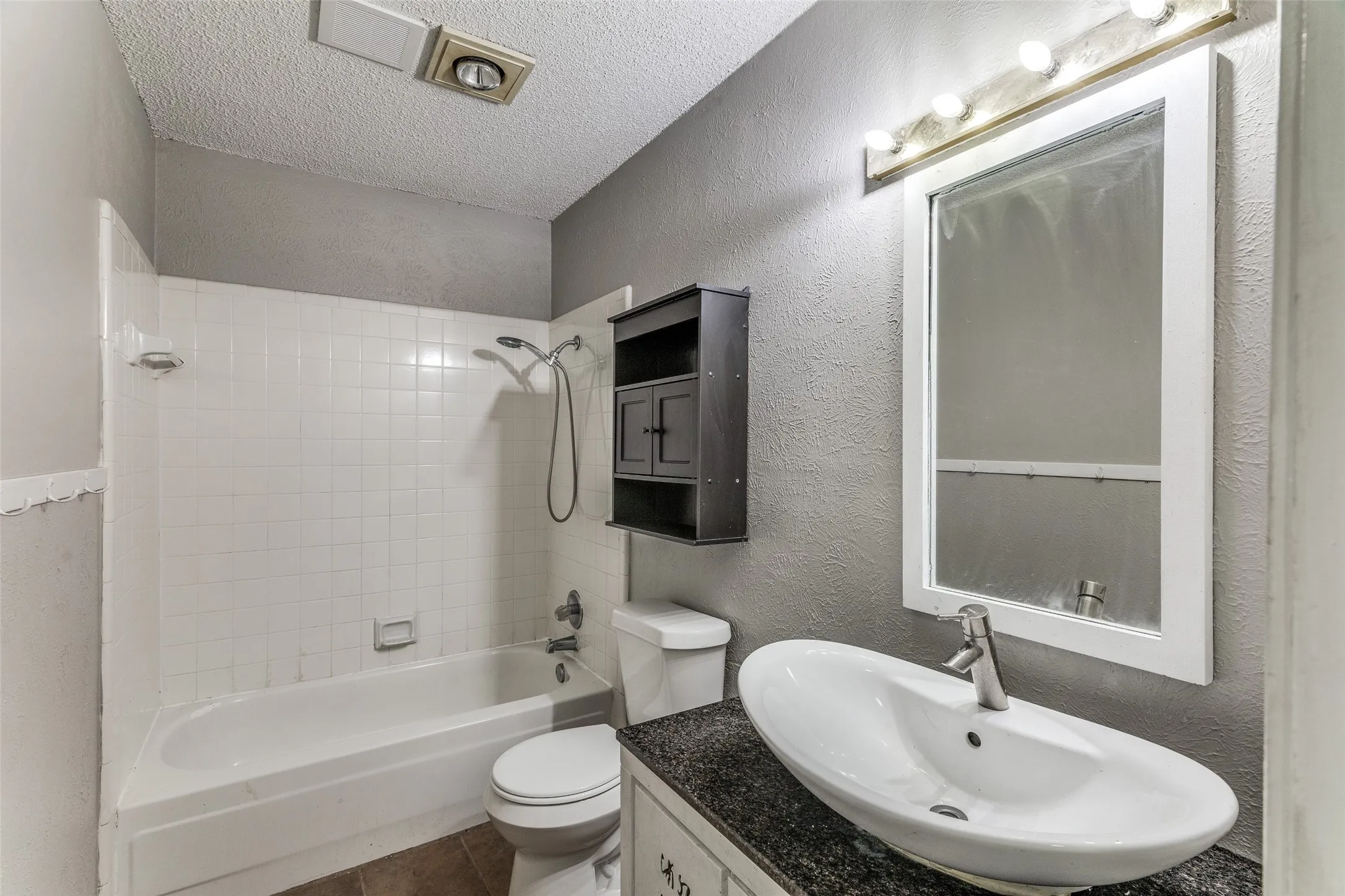 Bathroom with a white tiled shower, integrated bathtub, and a vessel sink set on a dark countertop