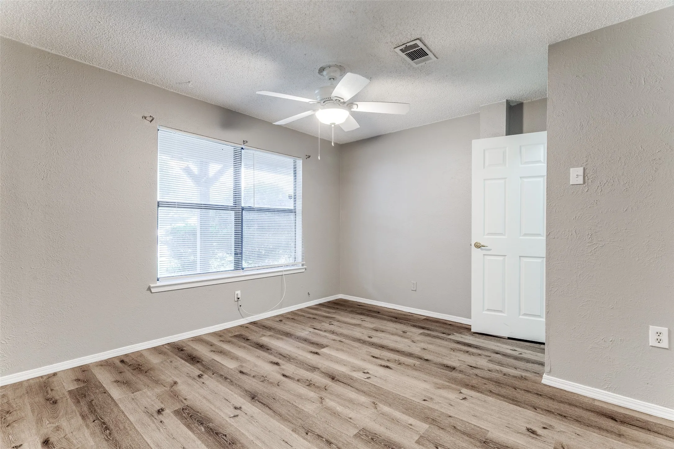 Wood-finish flooring, white paneled door, and a ceiling fan with integrated lighting