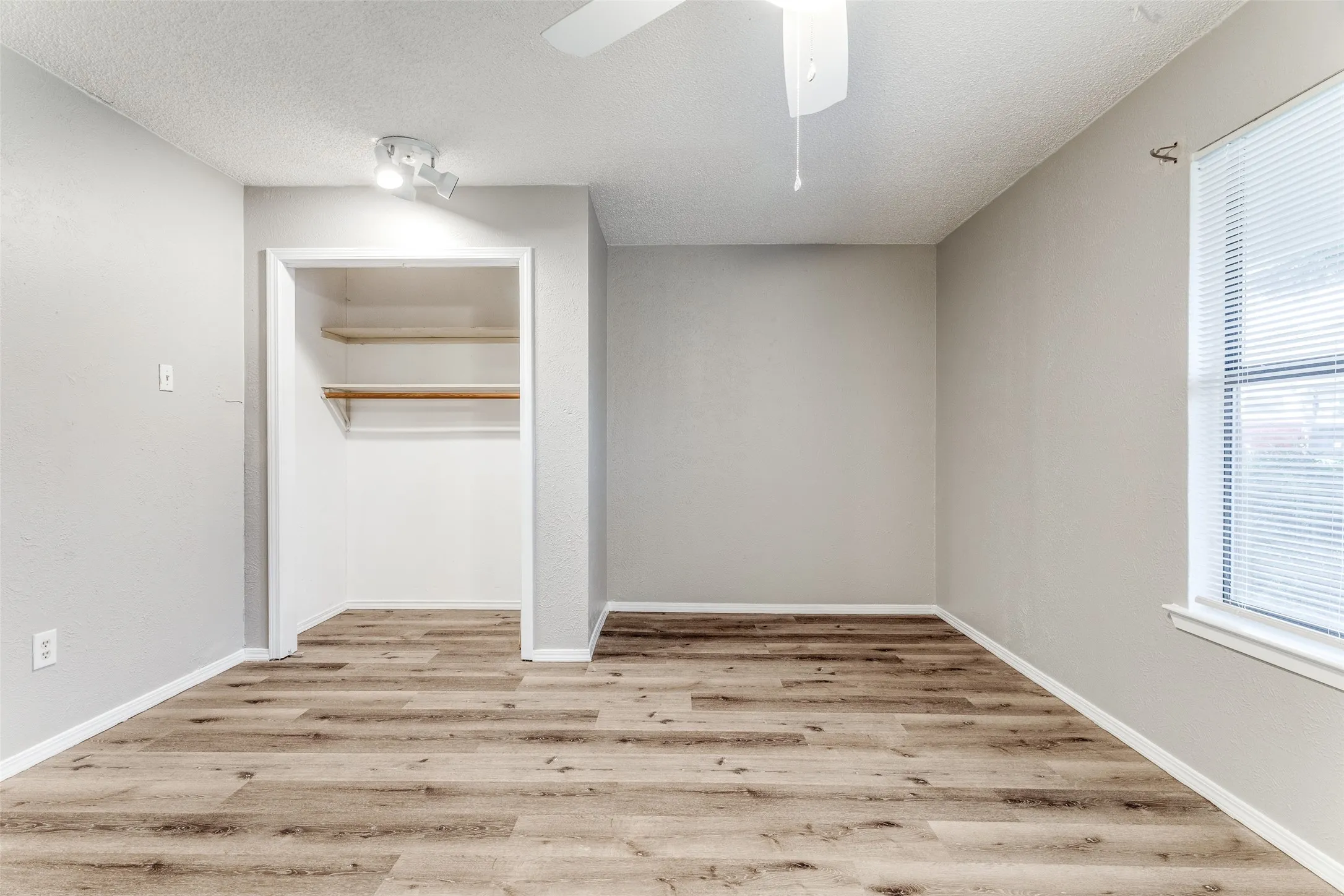 Wood-finish flooring, ceiling fan, track lighting, built-in shelving, window with blinds