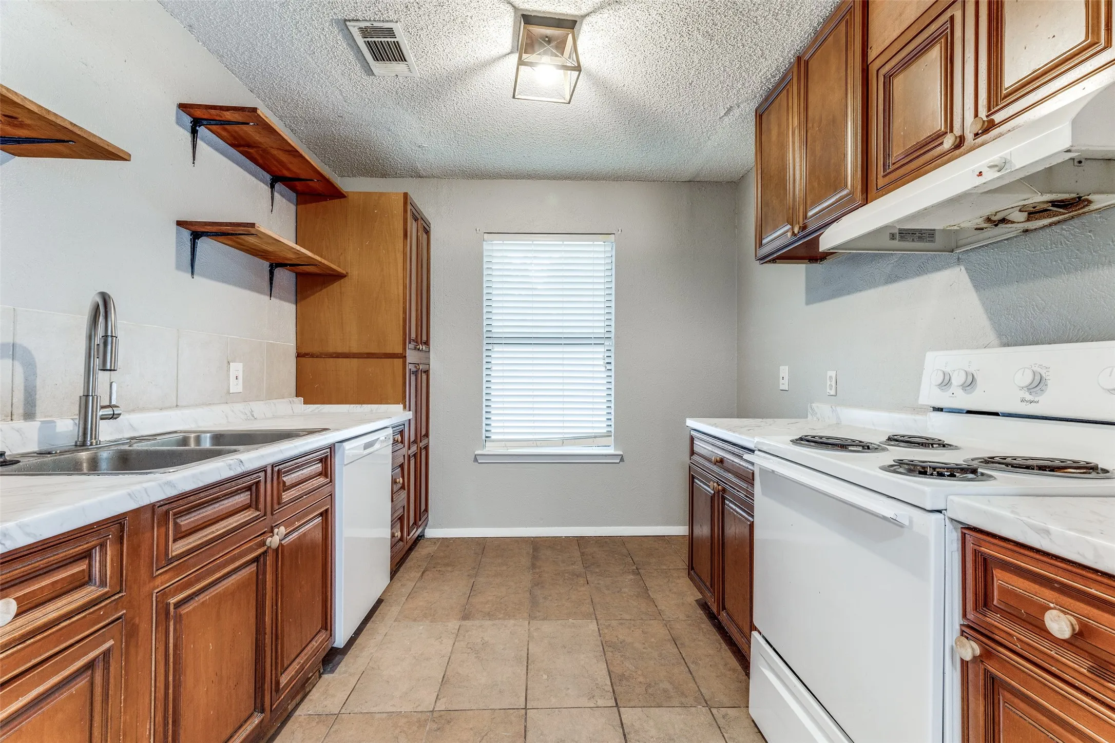 Kitchen featuring rich wood cabinetry, light-toned countertops, a stainless steel double-basin sink, and tile flooring