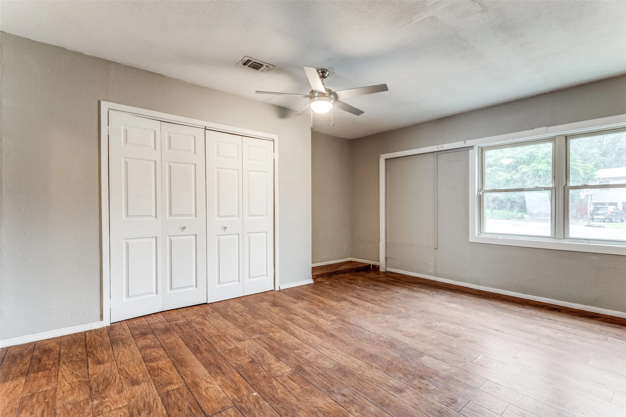 Wood-finish flooring throughout, bright walls, and a ceiling fan with integrated lighting