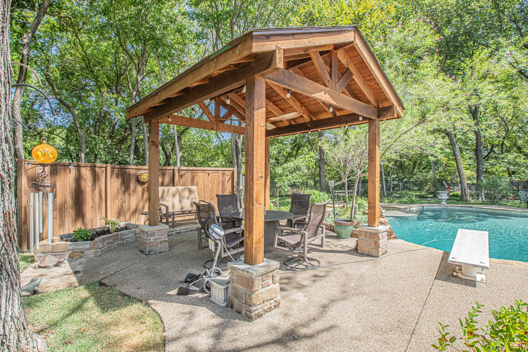Wood pergola with stone accents, expansive concrete patio, privacy fencing, stone planter, and inground swimming pool