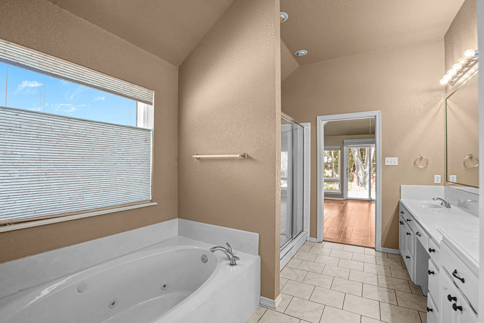 Soaking tub with chrome fixtures, dual vanity with white cabinetry, tile flooring, and a glass-enclosed shower