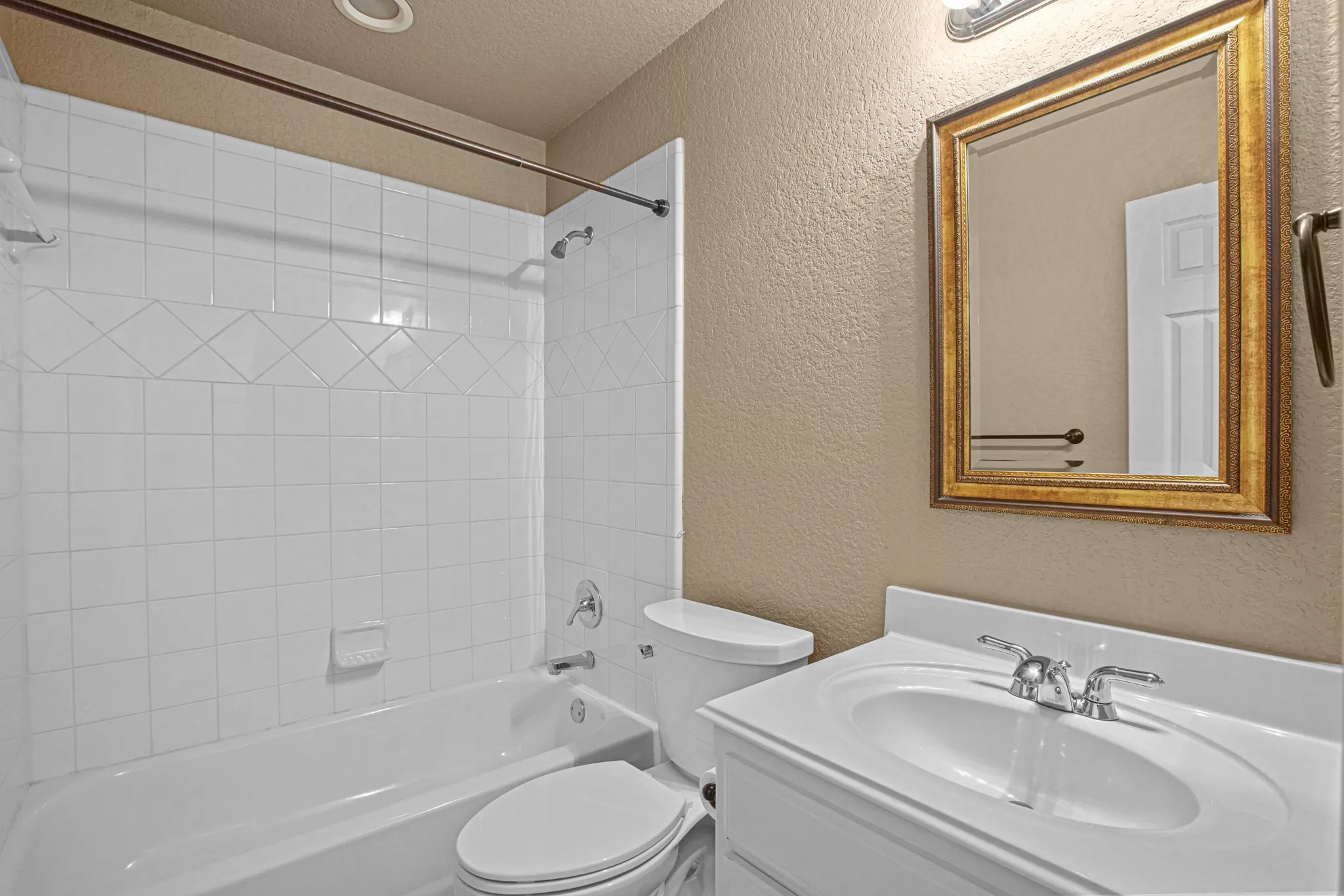 Bathtub with white tile surround, vanity with integrated sink, and framed wall mirror