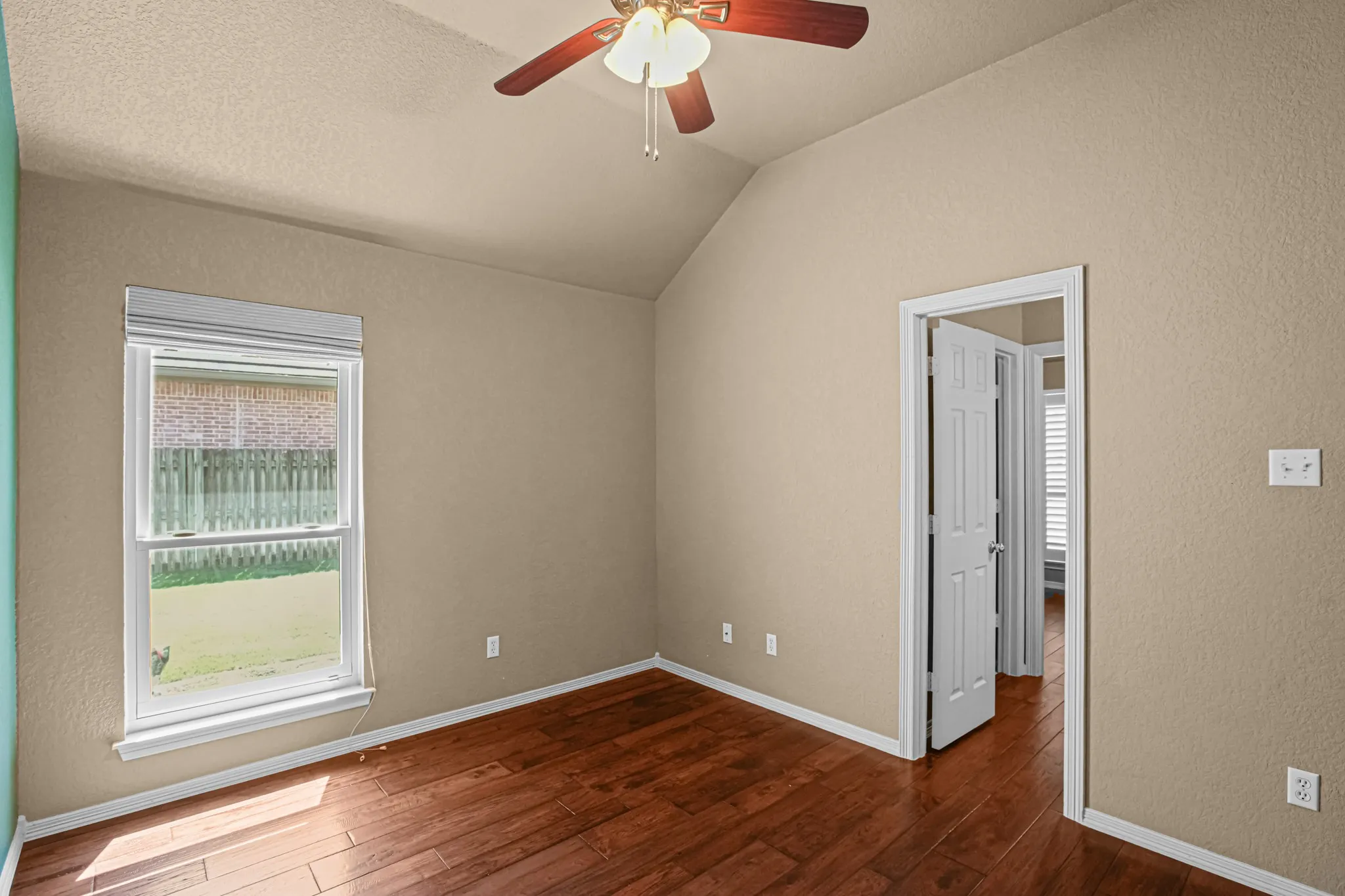 Vaulted ceiling featuring a ceiling fan, wood-finish flooring, and a white framed window