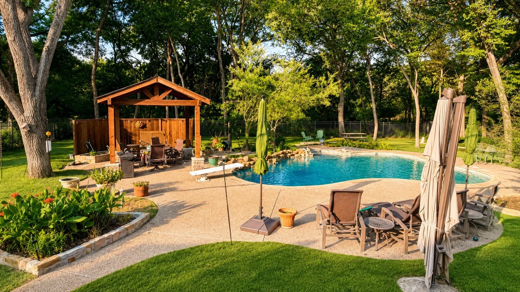 Freeform swimming pool with rock waterfall feature, exposed aggregate concrete patio, wood-frame gazebo, and surrounding mature trees