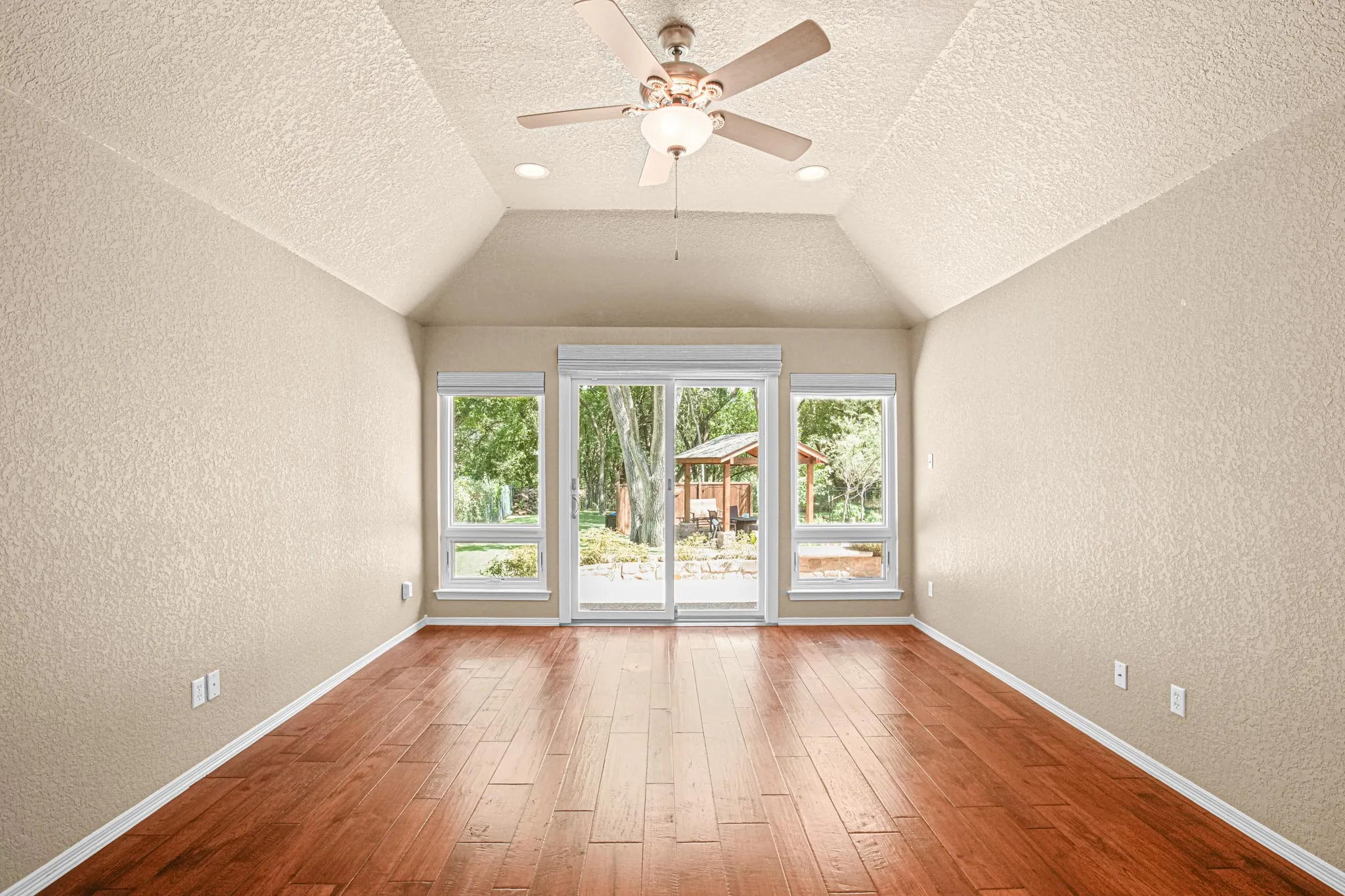 Vaulted ceiling with a ceiling fan, recessed lighting, wood-finish flooring, and sliding glass door with side windows