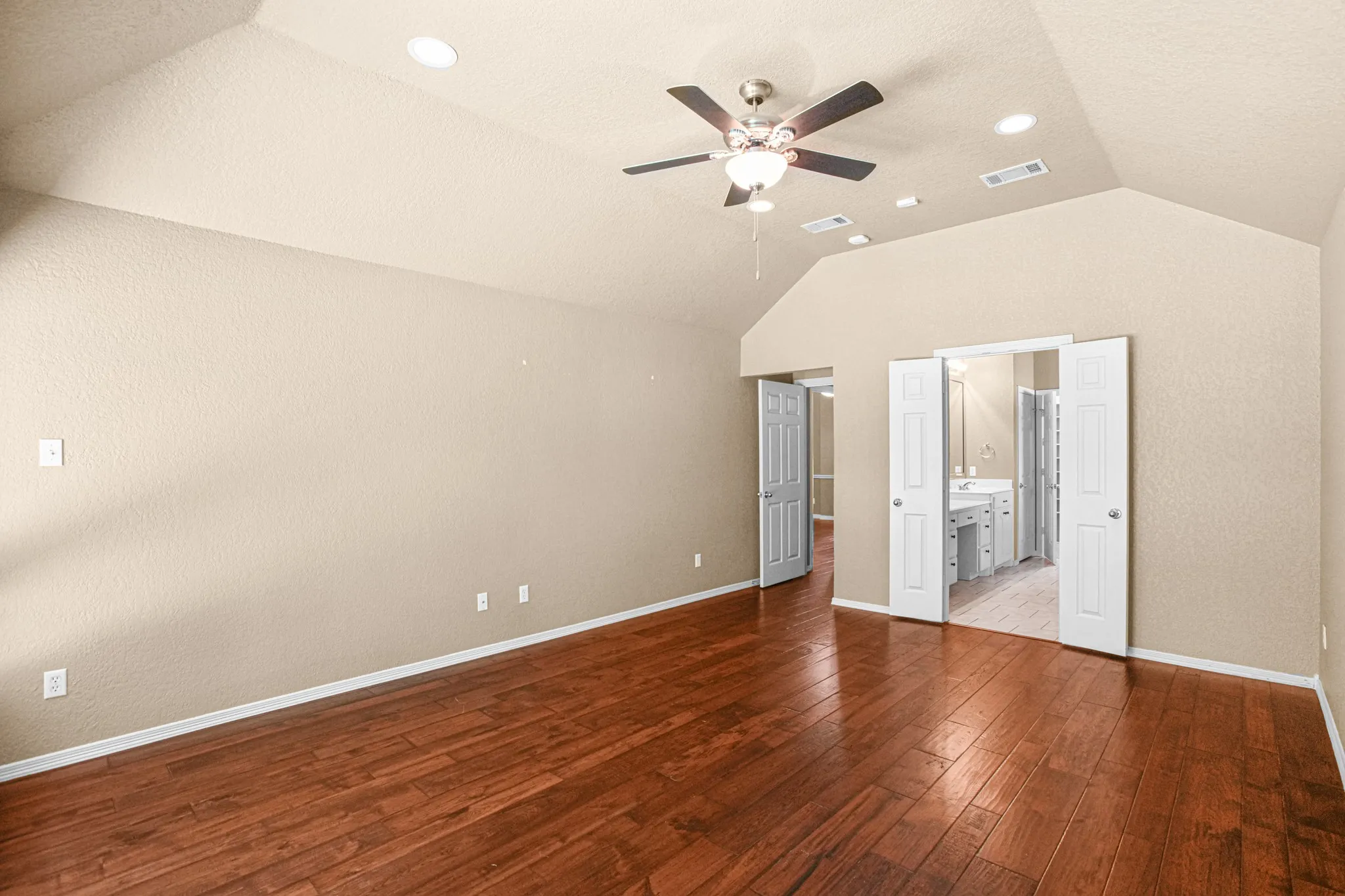 Vaulted ceilings, wood-finish flooring, ceiling fan, recessed lighting, and double-door access to an attached bath