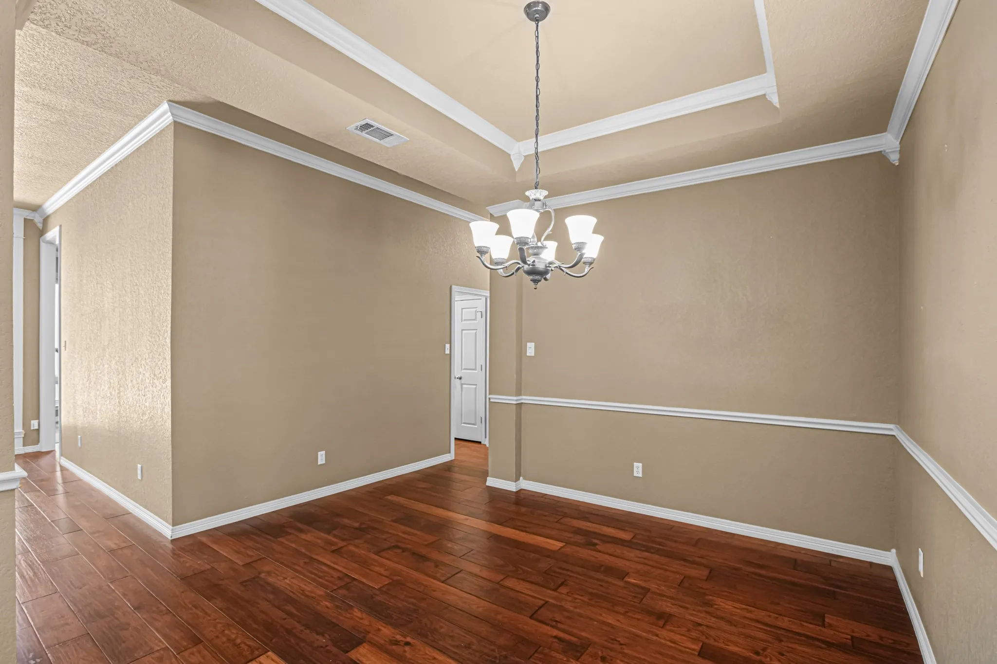 Tray ceiling with crown molding, chandelier, wood-finish flooring, and chair rail molding