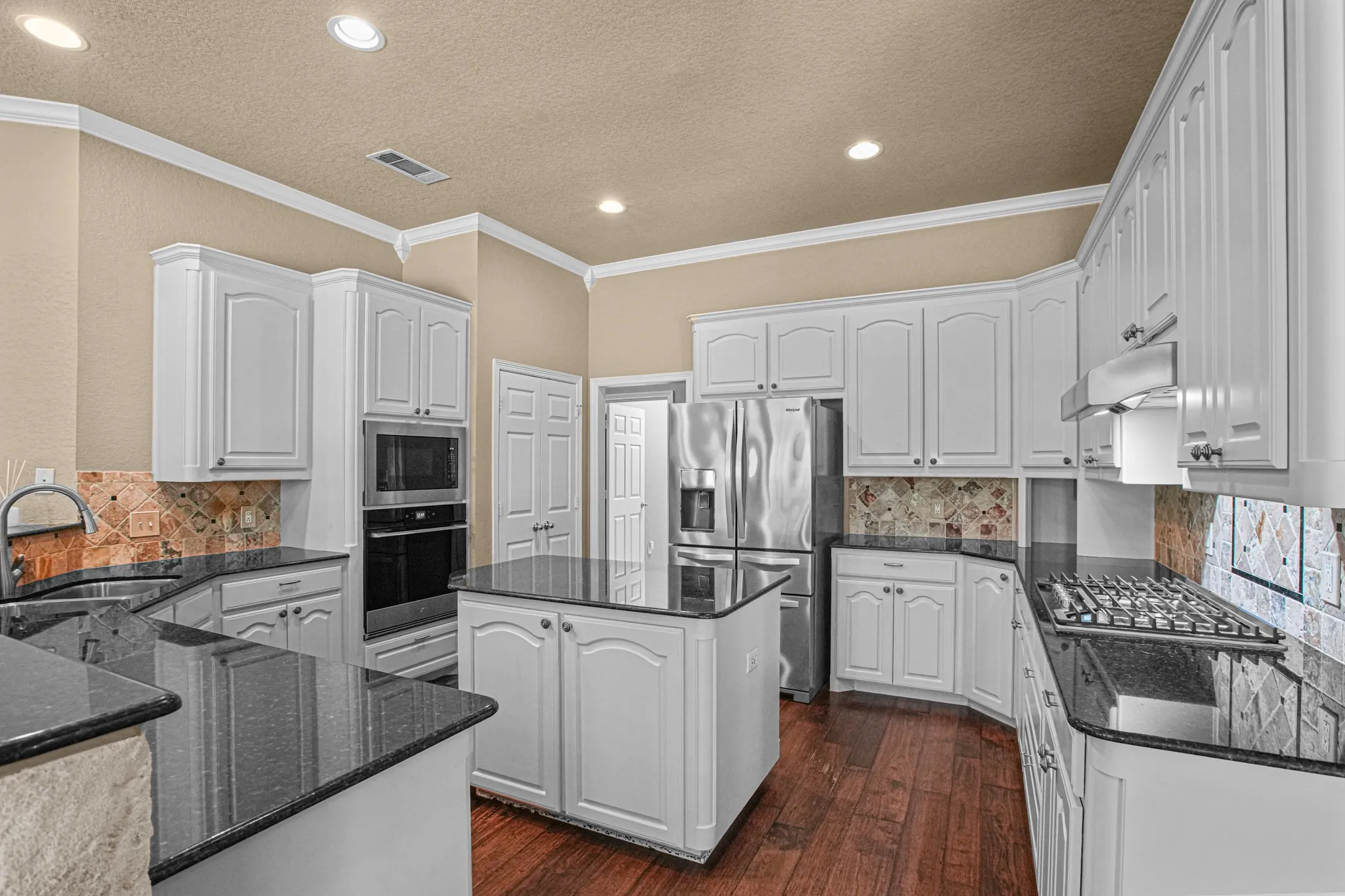 Wood-finish flooring, white cabinetry, dark countertops, and stainless steel appliances