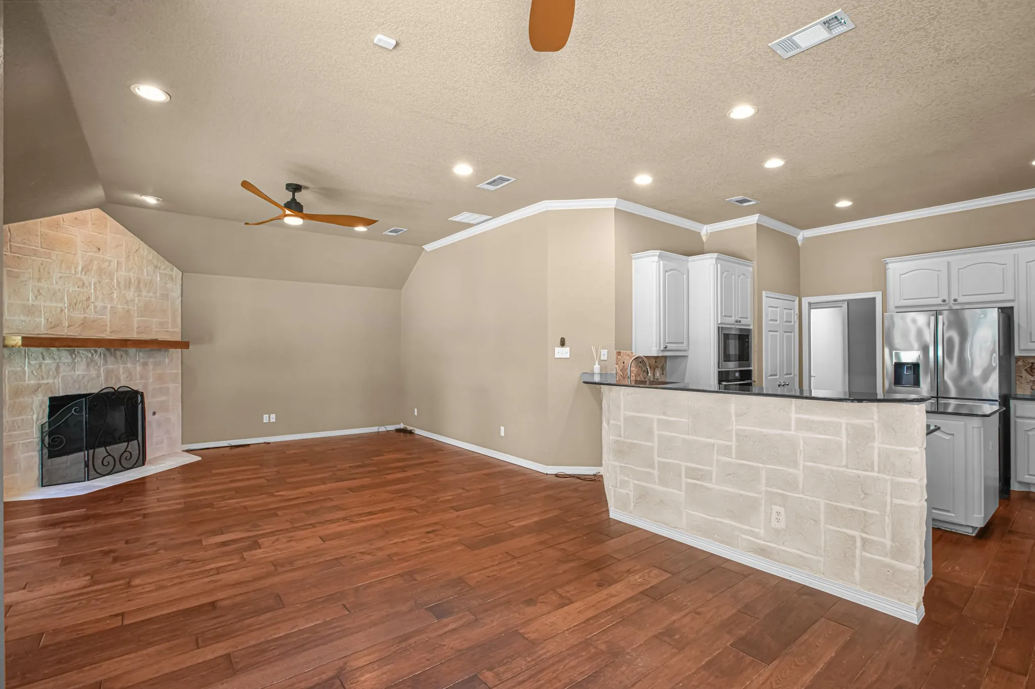 Hardwood flooring, vaulted ceiling, stone-clad fireplace with mantel, stone-clad breakfast bar, and white cabinetry