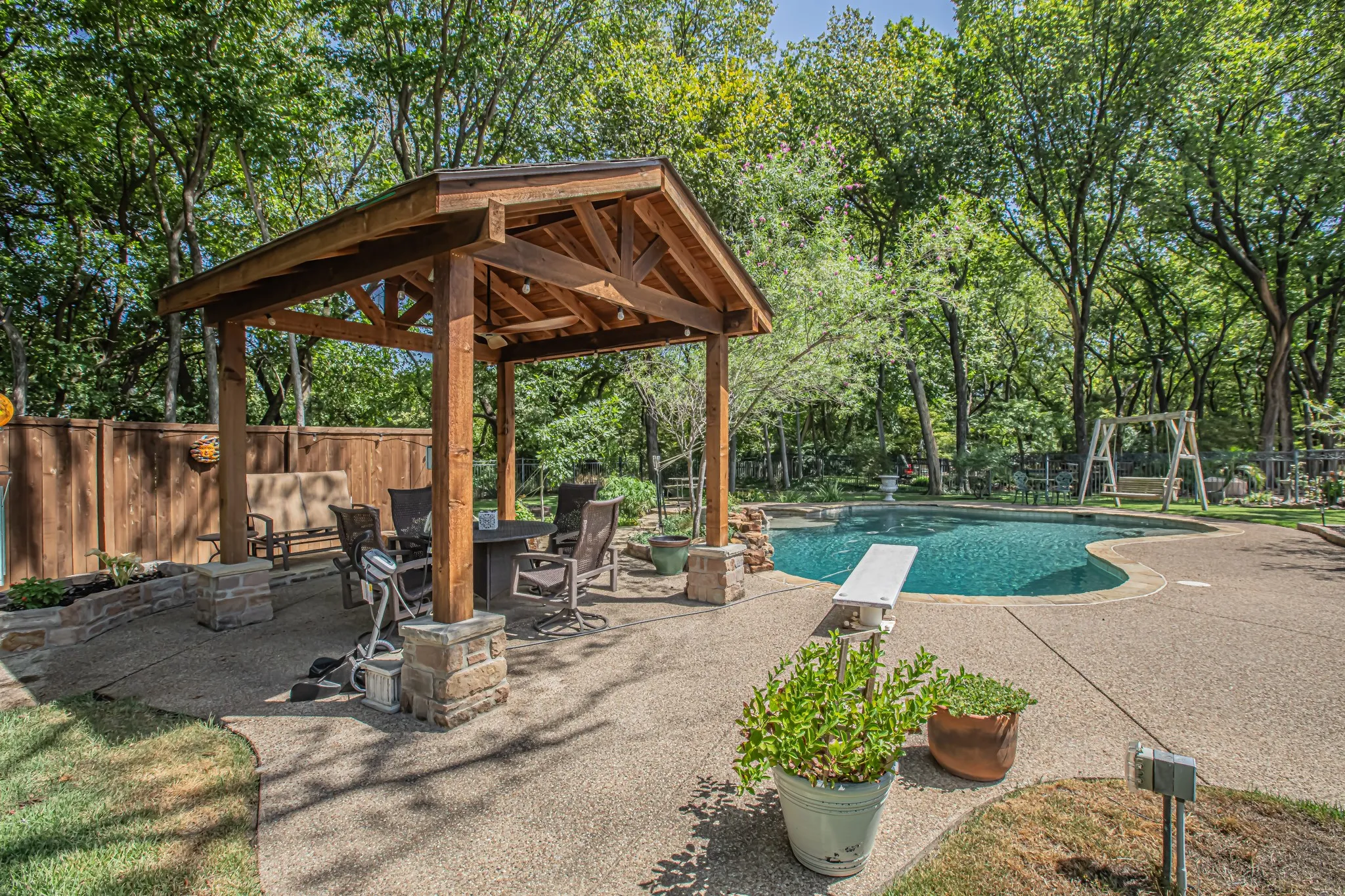 Expansive outdoor living area featuring a custom wood-framed pavilion, a freeform swimming pool with a diving board, and a privacy fence
