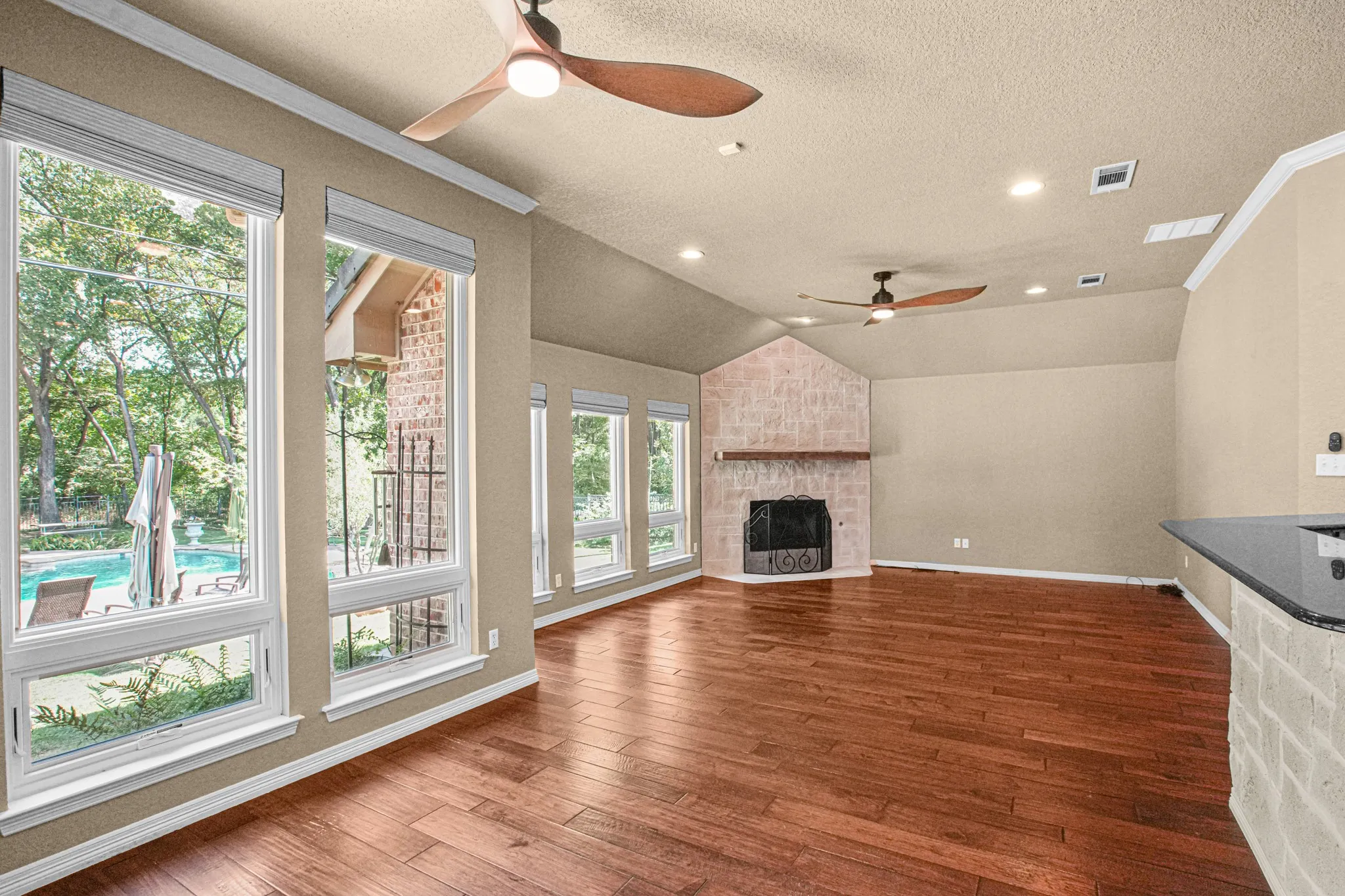 Vaulted ceiling with recessed lighting, wood-finish flooring, stone-clad fireplace, black granite countertop, and multiple windows