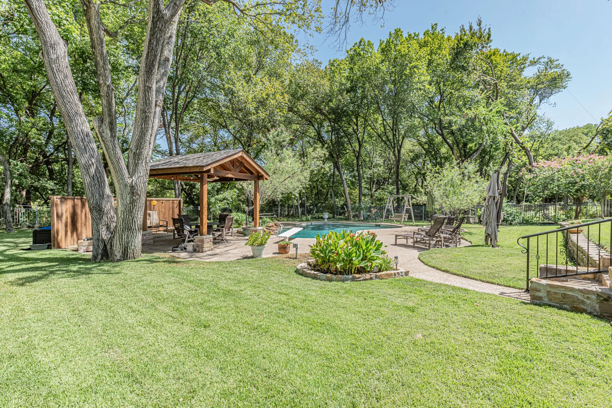Expansive green lawn with mature trees, a covered outdoor patio, and a swimming pool
