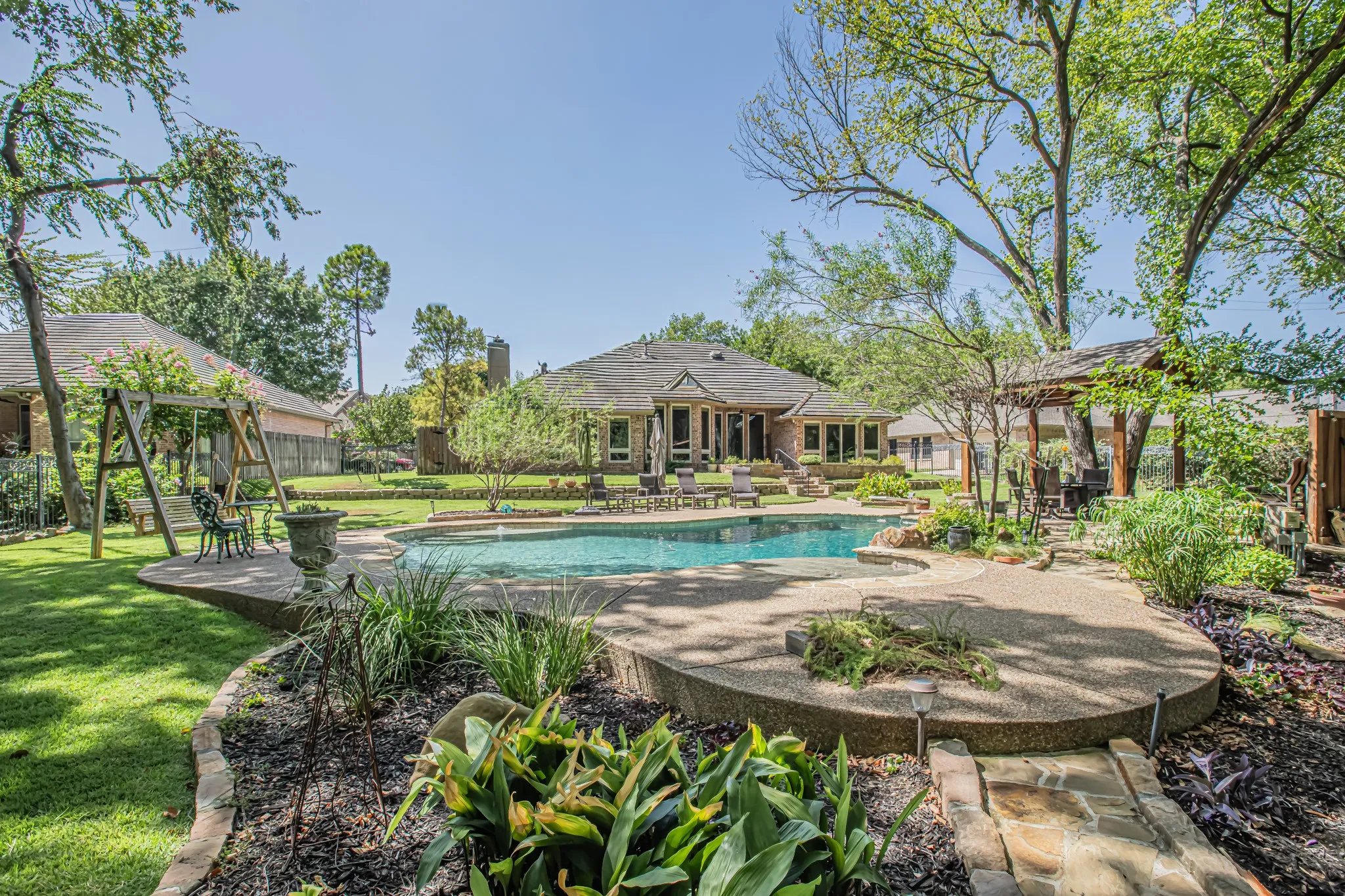 Expansive backyard featuring a large swimming pool, surrounding concrete patio, and lush landscaping