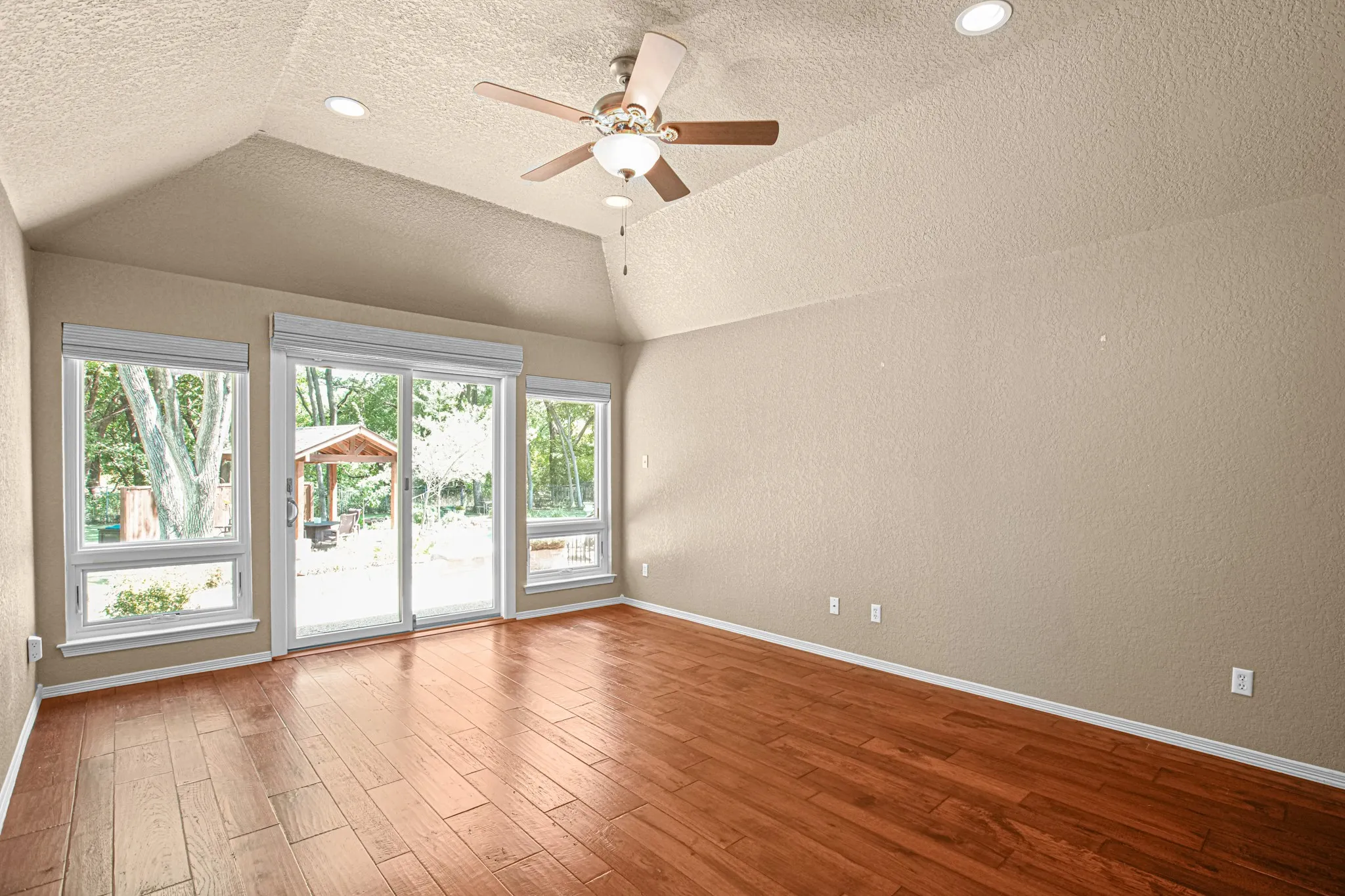 Vaulted ceiling with recessed lighting, wood-finish flooring, sliding glass door, multiple windows, and a ceiling fan