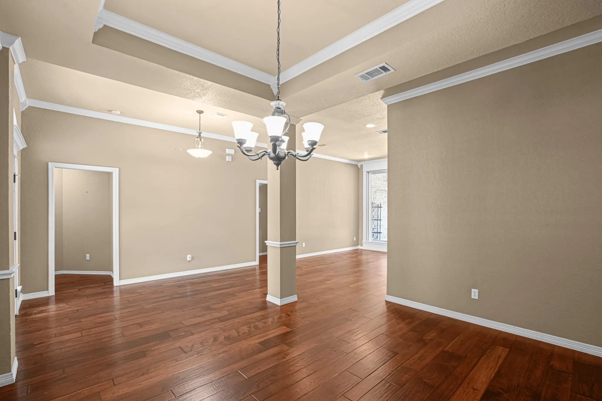 Wood-finish flooring throughout, tray ceiling with crown molding, chandelier, recessed lighting, and wall sconces